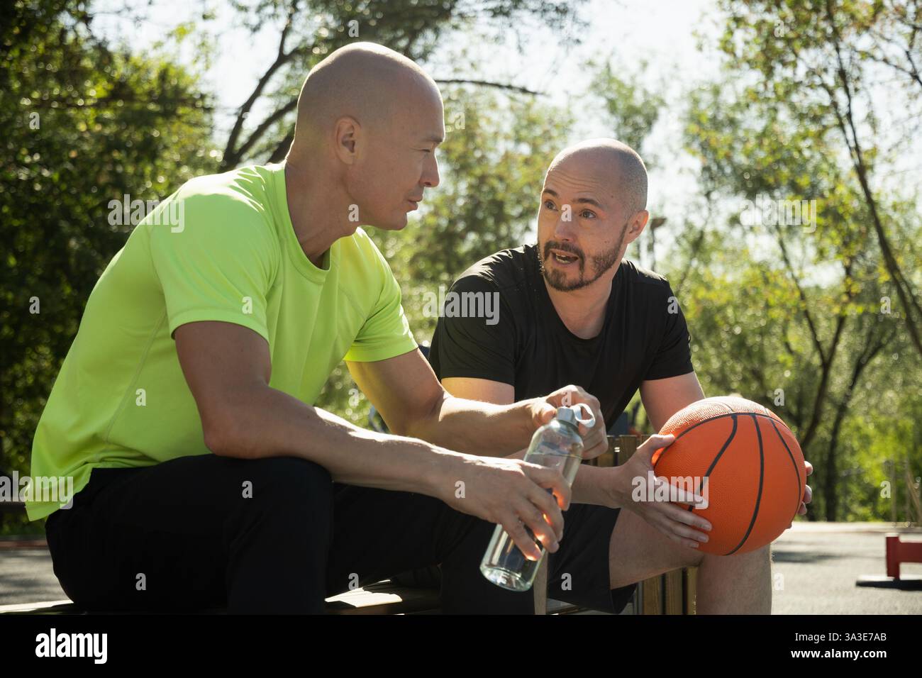 Due giocatori di pallacanestro seduti sulla panchina e che discutono di una partita sul campo sportivo. Competizione sportiva. Allenamento all'aperto. Sport di squadra. Foto Stock