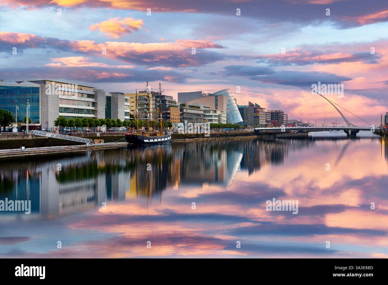 Gli edifici moderni fiancheggiano il fiume Liffey a Dublino, Irlanda, e l'iconico Samuel Beckett Bridge, a forma di arpa, si estende lungo il fiume. Foto Stock