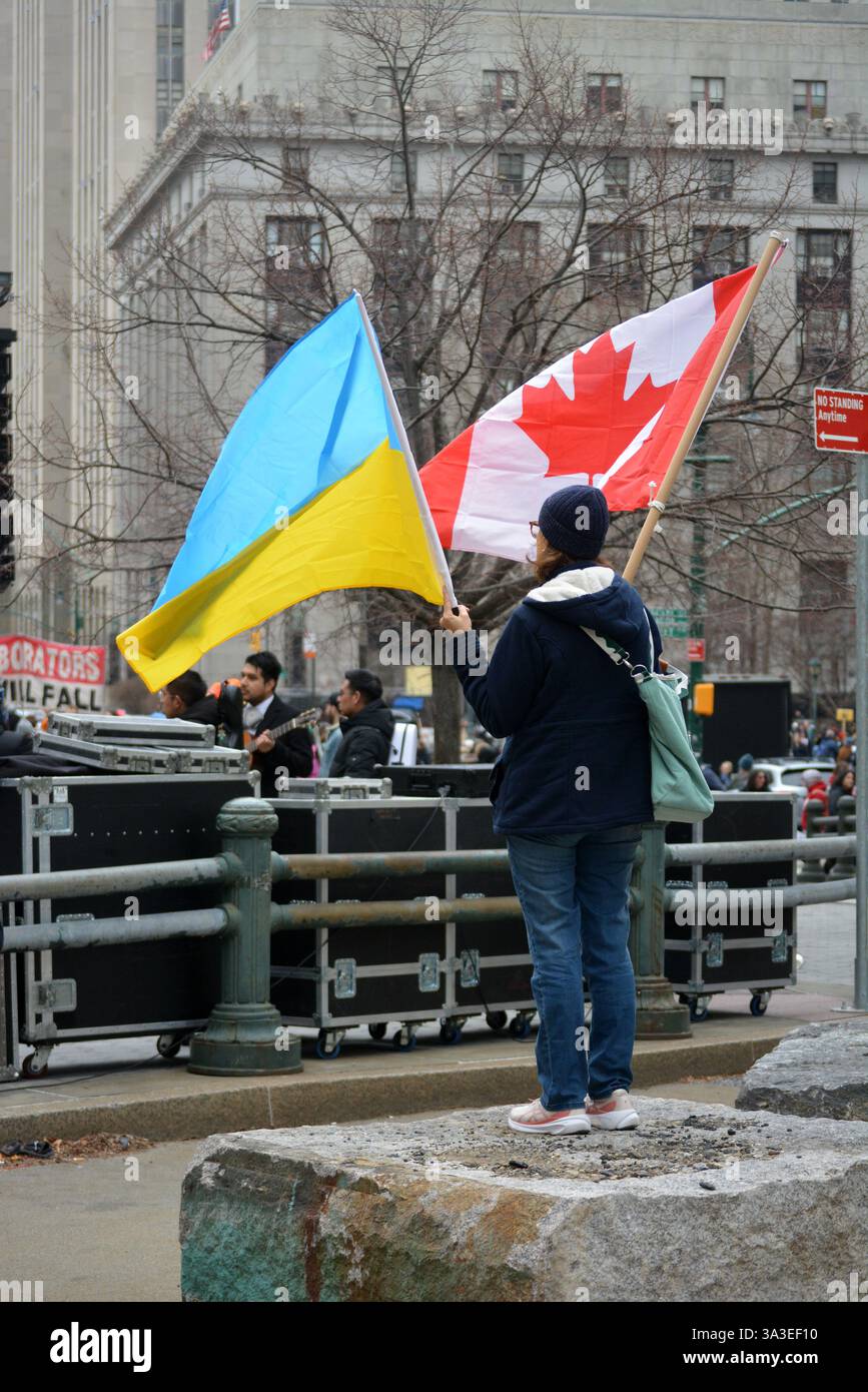 Persona che sventola bandiere canadesi e ucraine in una manifestazione Stop the Cuts contro i tagli DEL DOGE ai finanziamenti federali a Lower Manhattan. Foto Stock