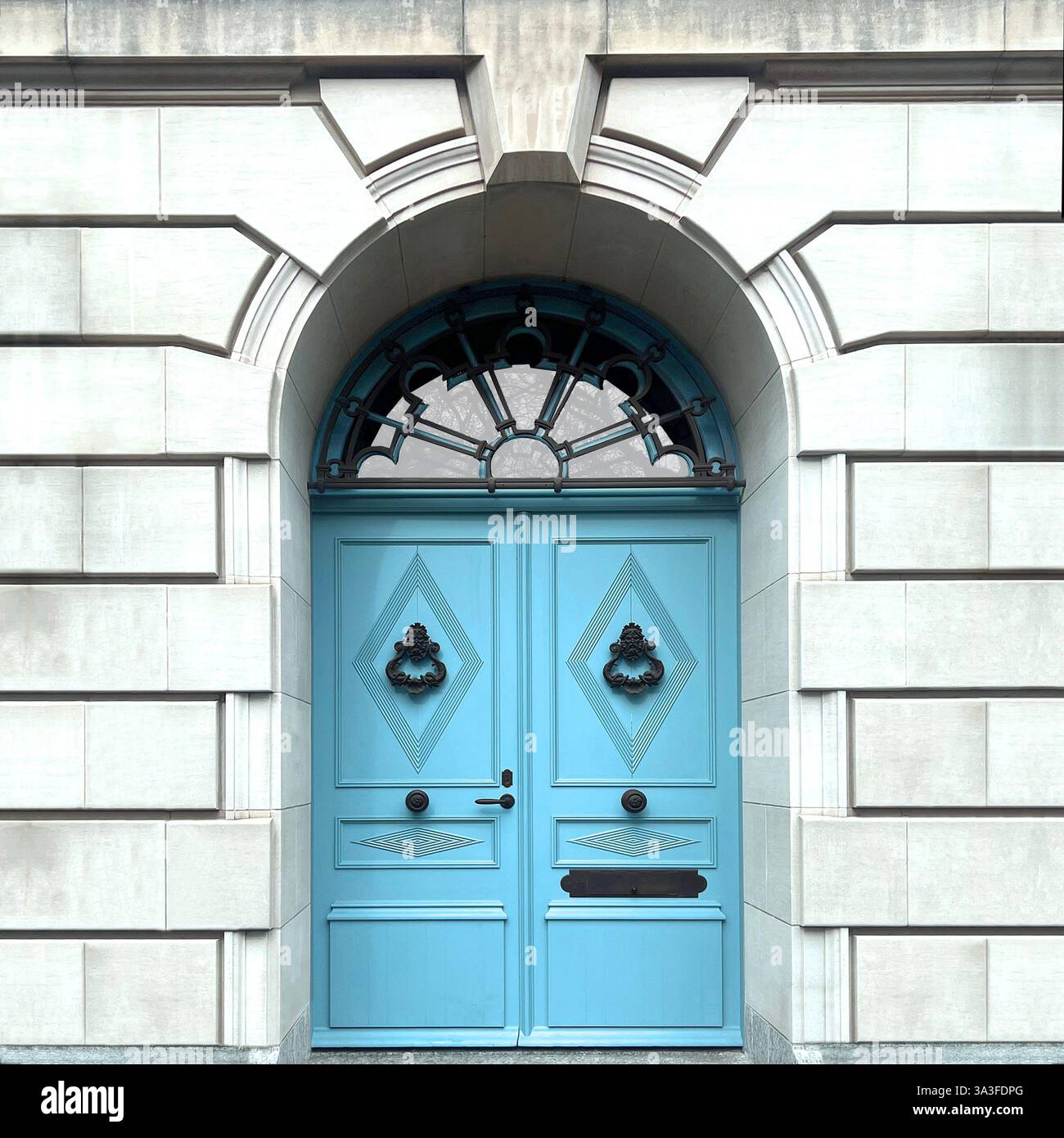 Eleganti doppie porte blu pastello poste all'interno di una grande entrata ad arco in pietra, caratterizzate da intricati lavori in ferro. - Immagine stock catturata con smartphone