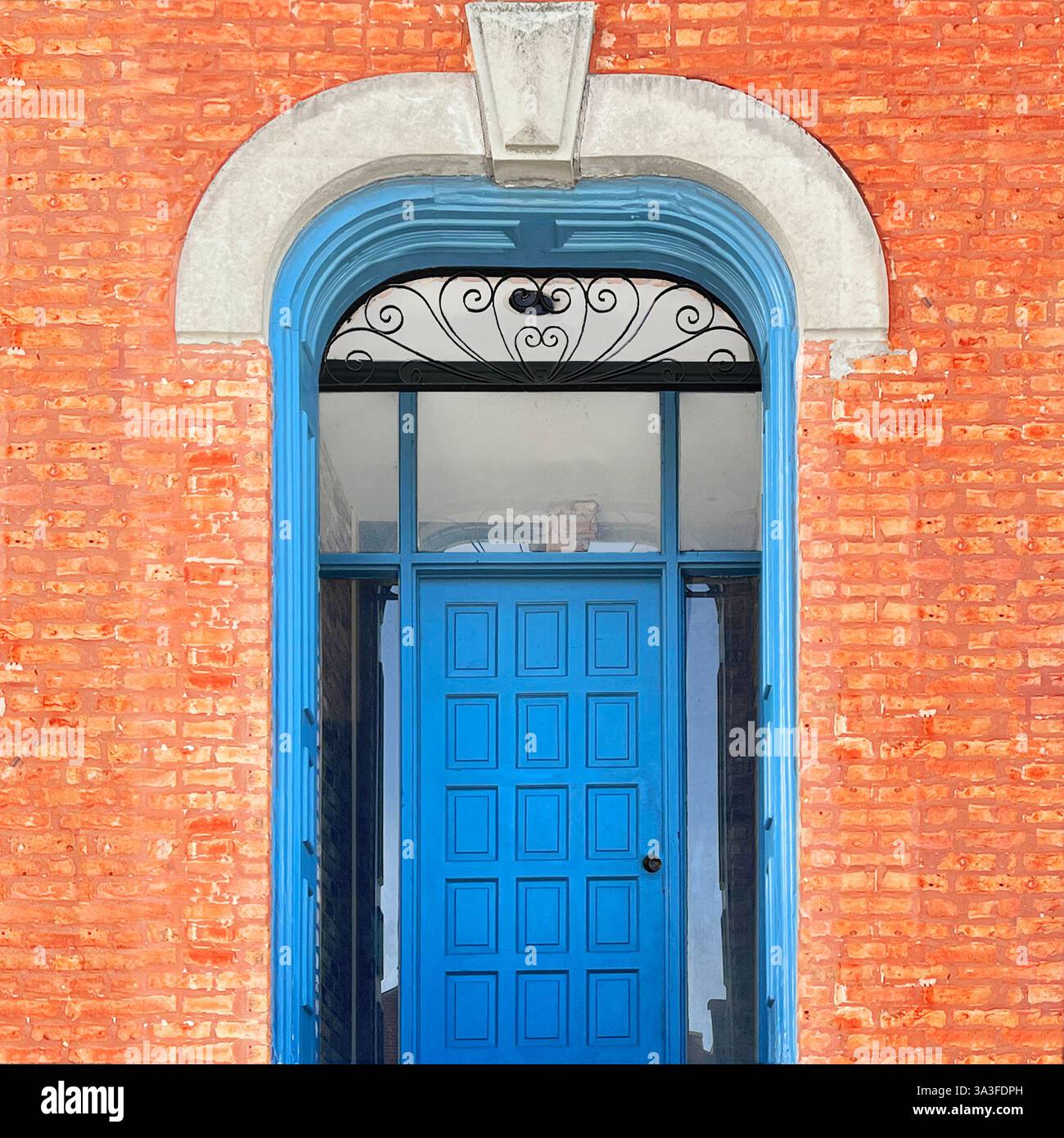 Porta in legno blu vibrante con intricato specchio di poppa in ferro, incorniciato da uno storico arco in mattoni rossi e dettagli in pietra. - Immagine stock catturata con smartphone