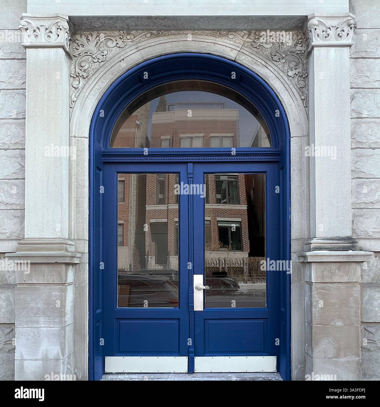 Eleganti doppie porte ad arco blu navy poste all'interno di una facciata in pietra ornata, con intricate incisioni e colonne. - Immagine stock catturata con smartphone