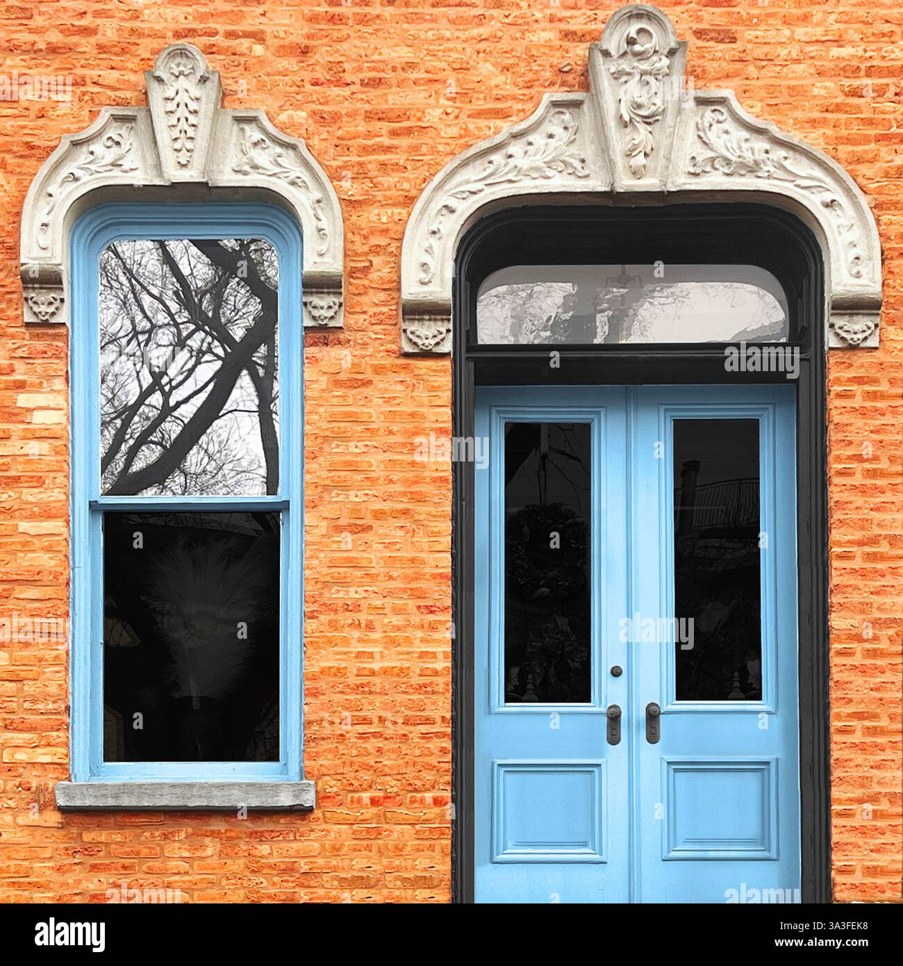 Eleganti porte doppie azzurre e cornice della finestra coordinata sono collocate in una calda facciata in mattoni arancioni, con archi in pietra ornati. - Immagine stock catturata con smartphone