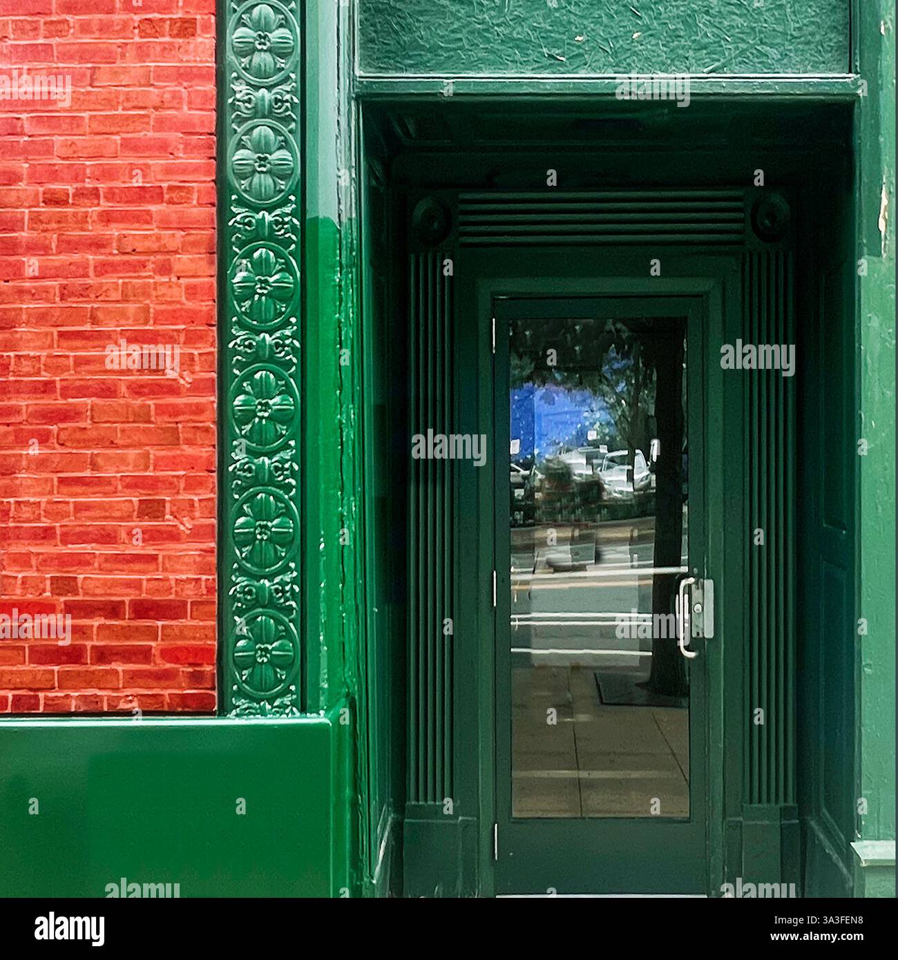 Porta di vetro verde all'interno, caratterizzata da decorazioni in metallo floreale, dettagli architettonici di verde intenso e una facciata in mattoni rossi. - Immagine stock catturata con smartphone