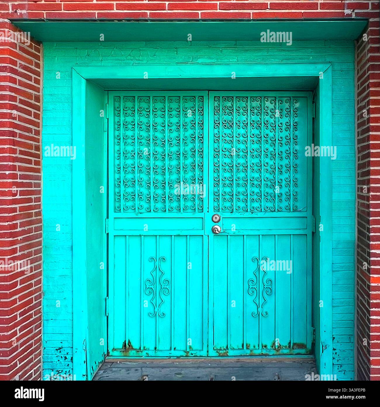 Vibranti porte doppie turchesi in ferro battuto con intricati lavori di scorrimento, che riflettono il tradizionale design asiatico, adagiate su una facciata in mattoni rossi. - Immagine stock catturata con smartphone