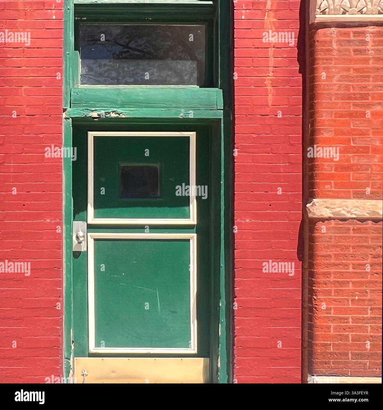 Una suggestiva porta verde incorniciata da un'audace facciata in mattoni rossi, che mostra un gioco di colori e texture contrastanti, in un ambiente urbano. Foto Stock