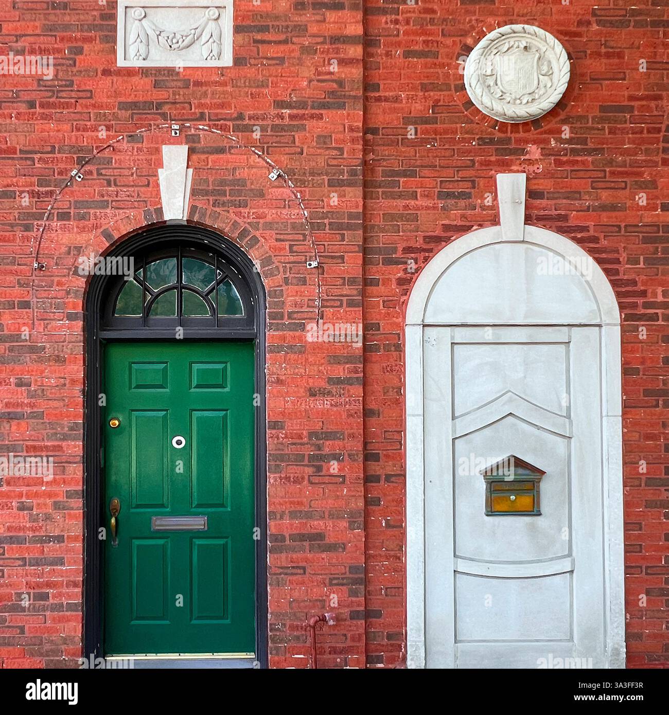 Porta ad arco verde posta in uno storico edificio di mattoni rossi accanto ad un ingresso decorativo sigillato. - Immagine stock catturata con smartphone