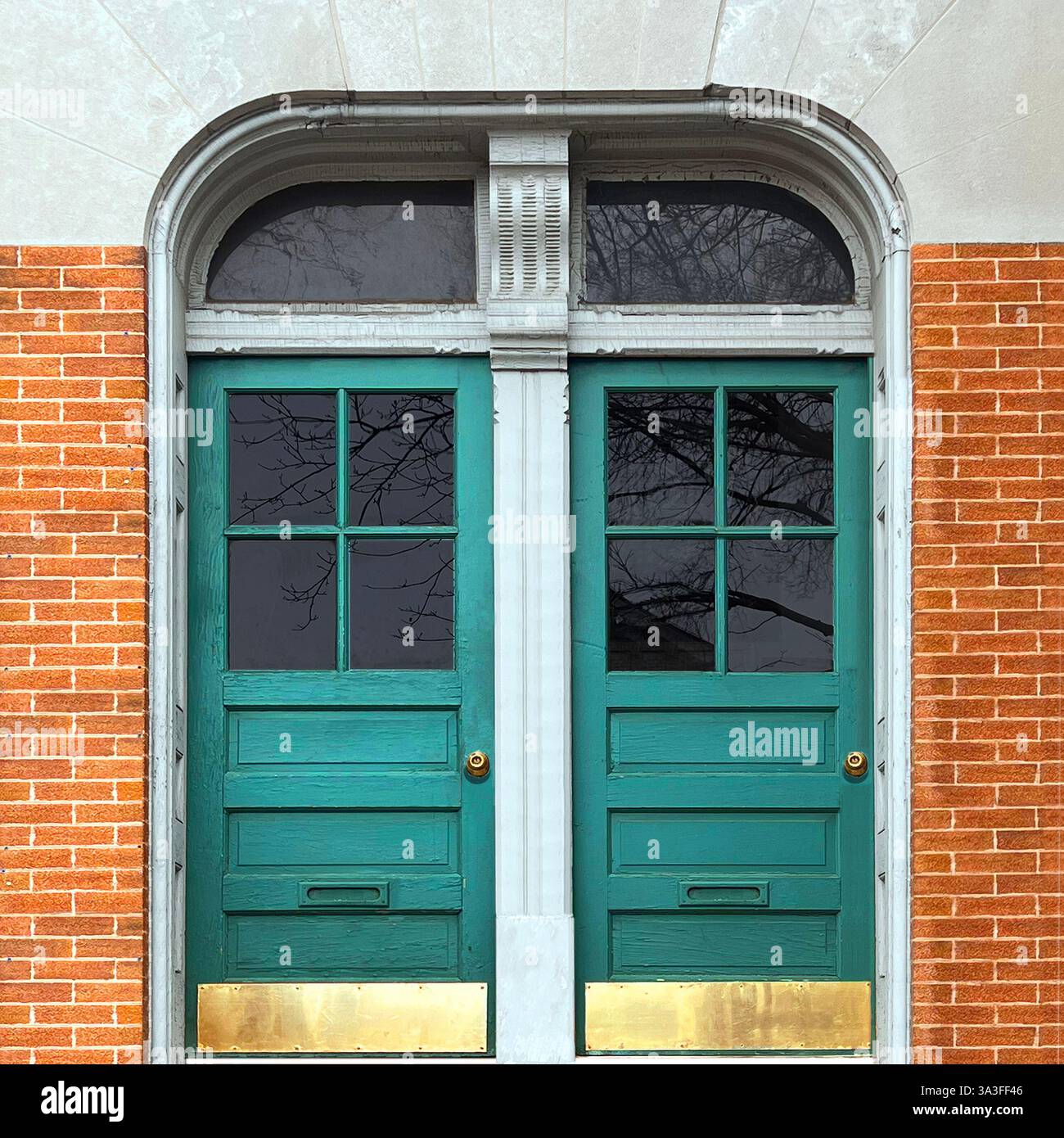 Eleganti porte doppie in color verde acqua con pannelli di vetro, incorniciate da una facciata ad arco in pietra e pareti in mattoni arancioni. Foto Stock
