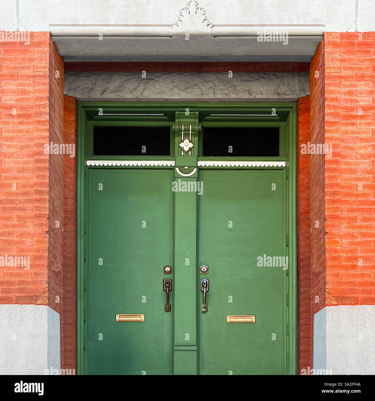 Eleganti porte doppie verdi con dettagli intricati e finestre sullo specchio di poppa, incorniciate da una facciata in mattoni arancioni e pietra. Foto Stock