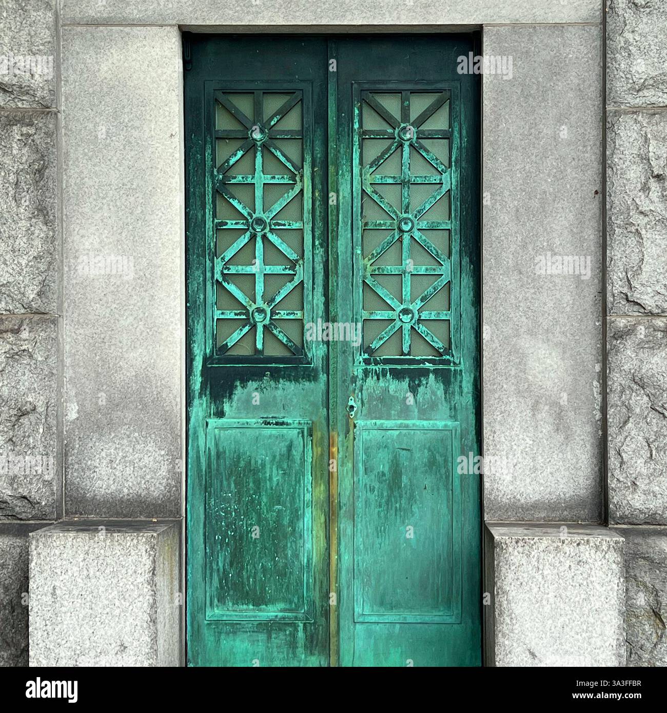 Una porta in mausoleo in bronzo con struttura geometrica a reticolo, situata all'interno di una tomba in pietra, che mostra una patina verde impressionante da anni di ossidazione. - Immagine stock catturata con smartphone