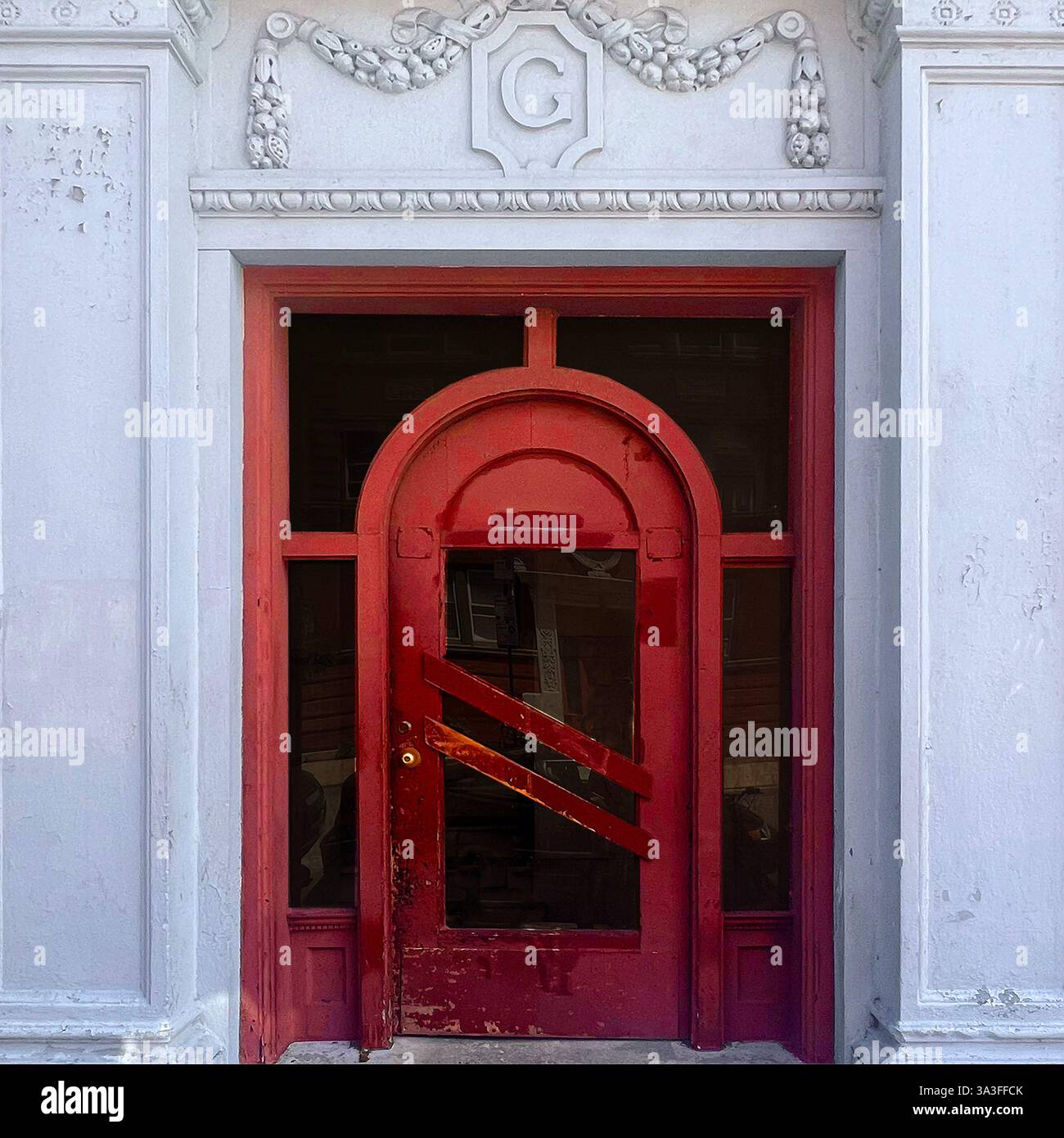 Una porta vintage ad arco rossa, adagiata all'interno di una facciata bianca ornata con dettagli e dettagli architettonici e un emblema decorativo "G" a Chicago. - Immagine stock catturata con smartphone