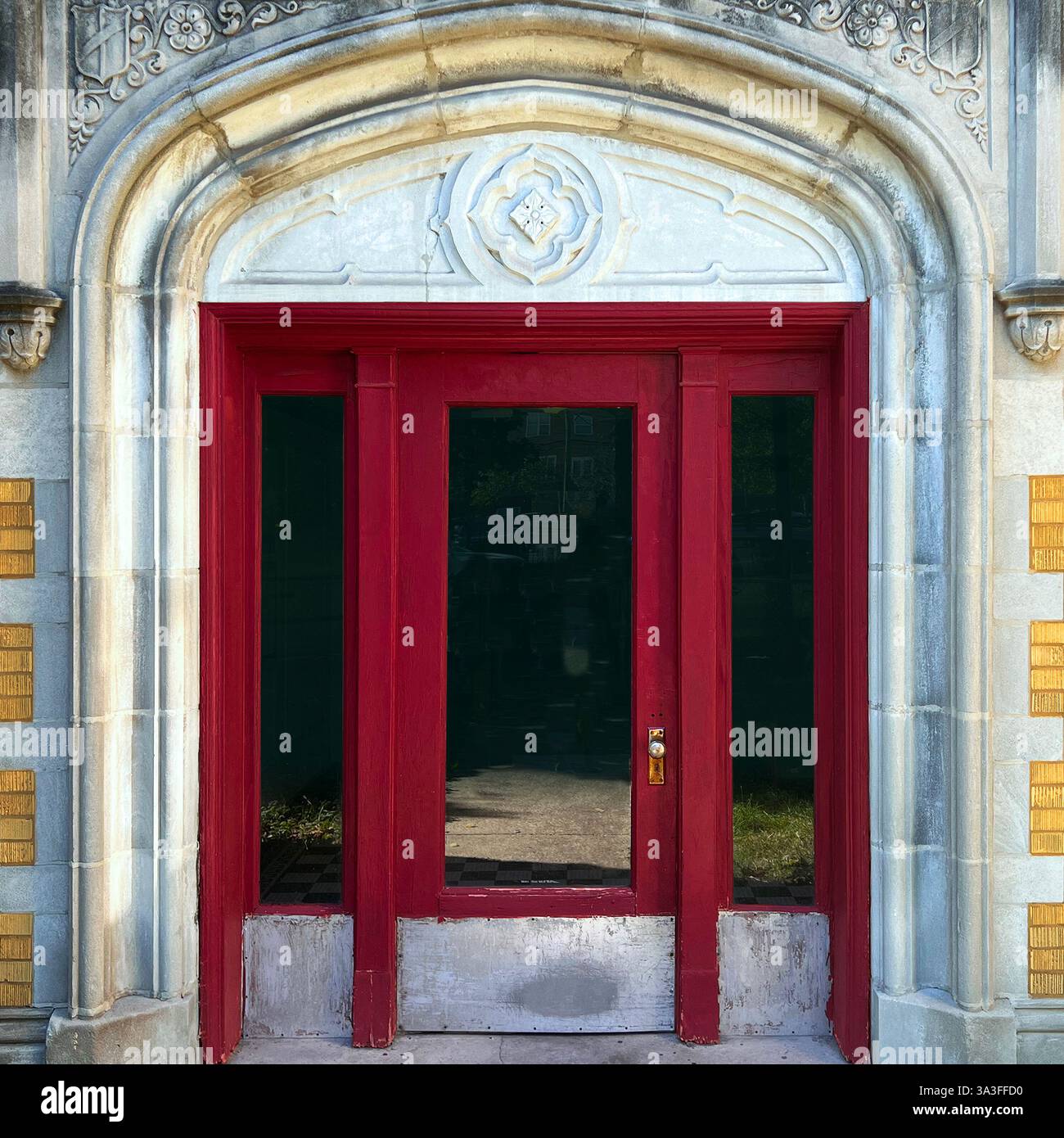 Una suggestiva porta rossa incorniciata da un elegante ingresso in pietra ad arco, adornata da intricate incisioni e accenti in mattoni dorati a Chicago. - Immagine stock catturata con smartphone