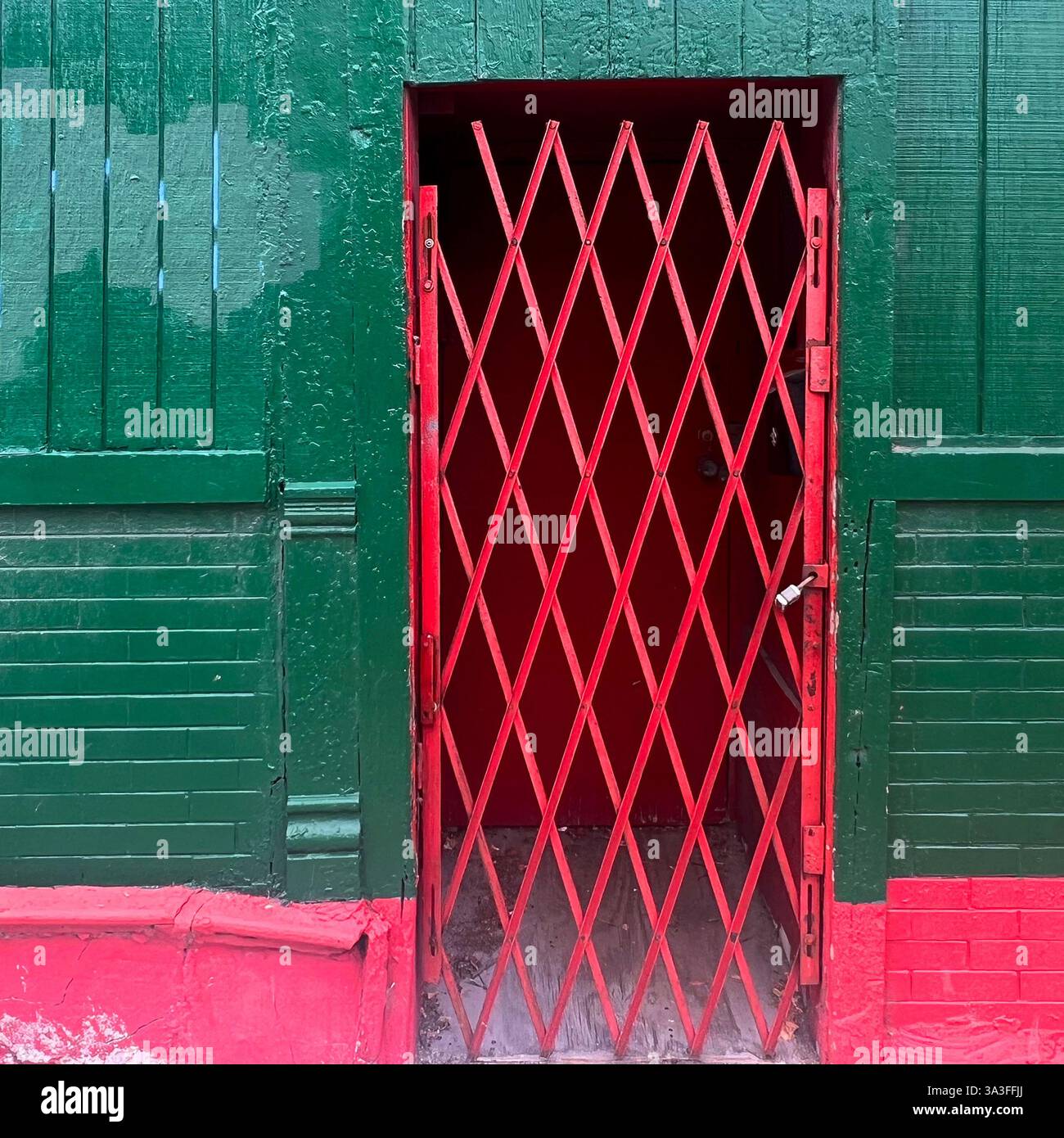 Il cancello di sicurezza rosso con un motivo a reticolo di diamanti protegge l'ingresso di un vivace edificio urbano dipinto di verde e rosso a Chicago Foto Stock