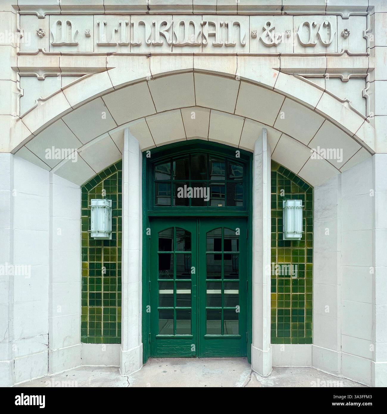 Una storica entrata verde a doppia porta con dettagli in pietra ad arco in stile gotico e accenti di piastrelle verdi. - Immagine stock catturata con smartphone