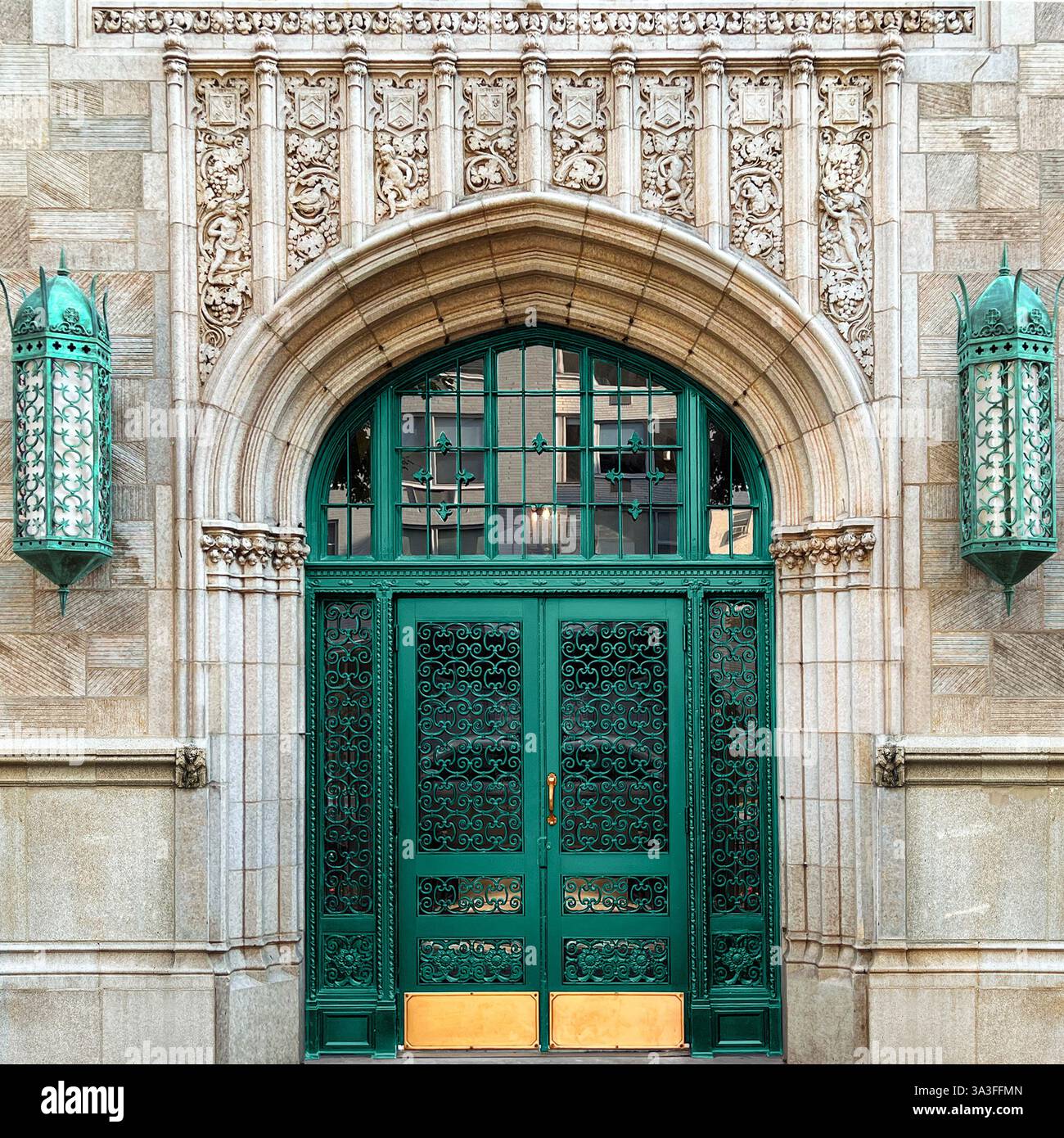 Porta in ferro battuto verde posta all'interno di un grande ingresso in pietra ad arco, adornata da intricati intagli in stile gotico e lanterne decorative. - Immagine stock catturata con smartphone