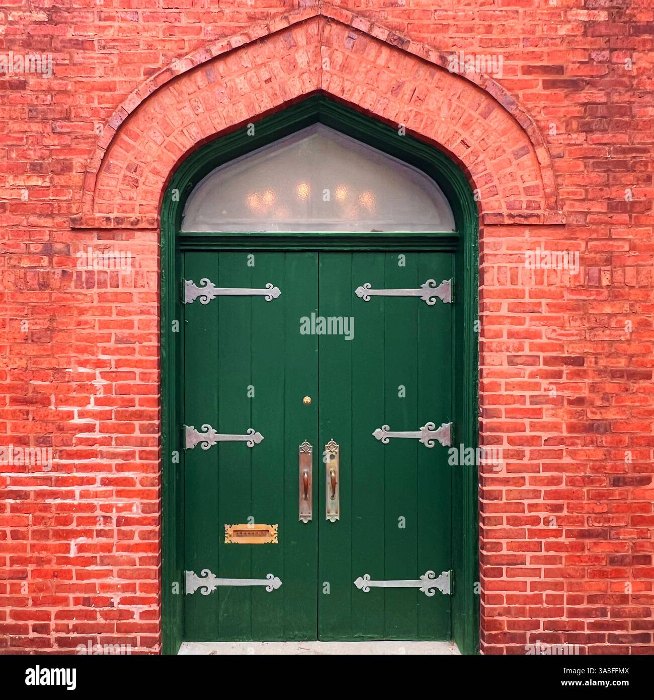 Una suggestiva porta doppia in legno verde con cerniere e maniglie in metallo ornato, adagiata all'interno di un arco in mattoni di stile gotico di uno storico edificio in mattoni rossi. - Immagine stock catturata con smartphone