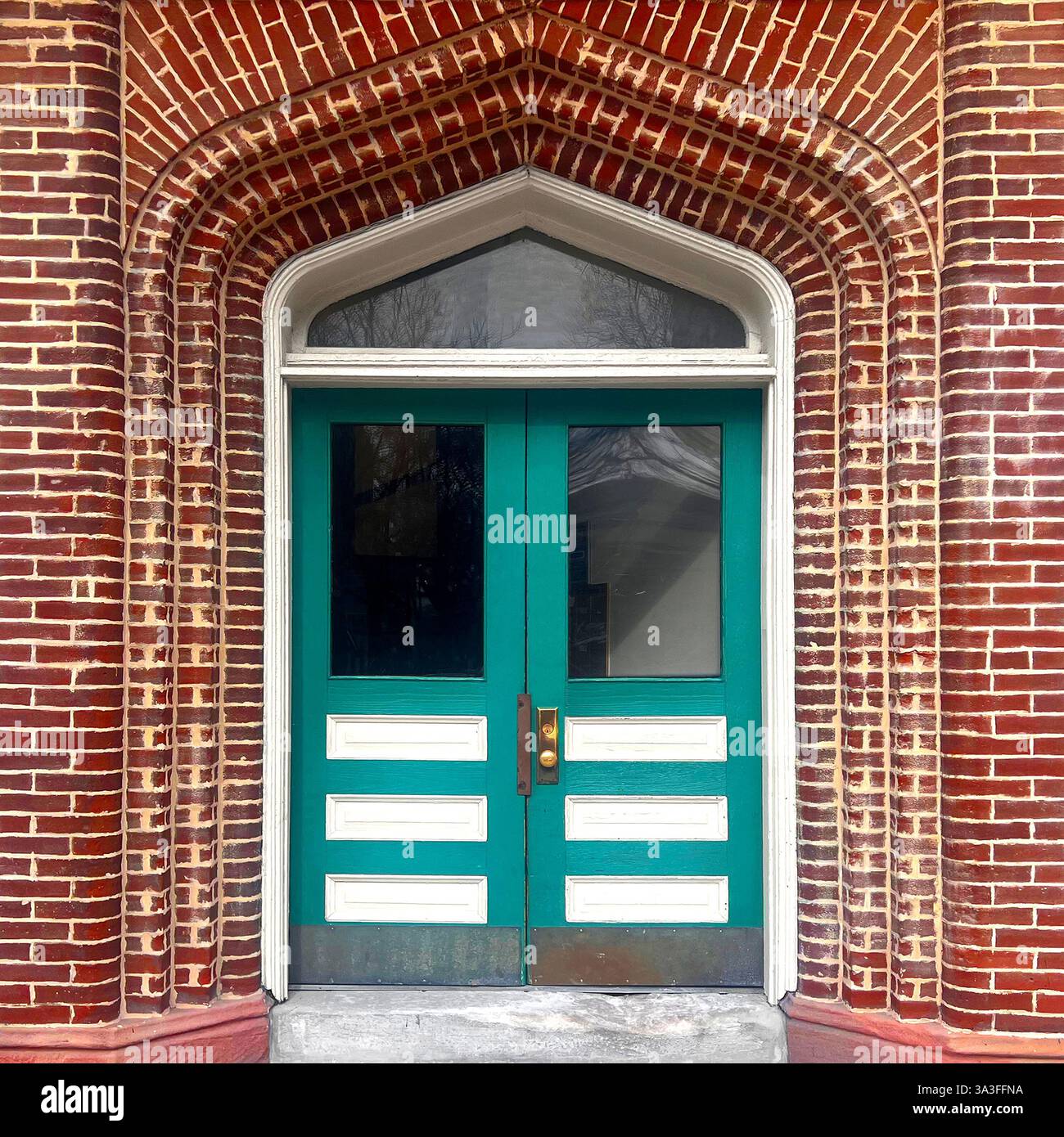 Porta doppia vintage verde e bianca all'interno di un ingresso in mattoni ad arco in stile gotico che mostra intricati lavori in mattoni. - Immagine stock catturata con smartphone