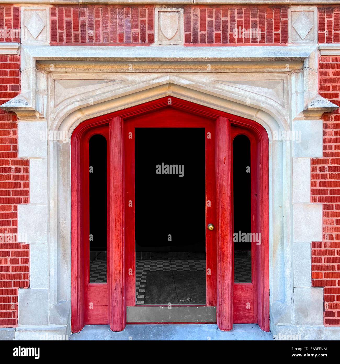Porta rossa in stile gotico, incorniciata da intricati dettagli in pietra calcarea, adagiata all'interno della facciata dell'edificio in mattoni rossi. - Immagine stock catturata con smartphone