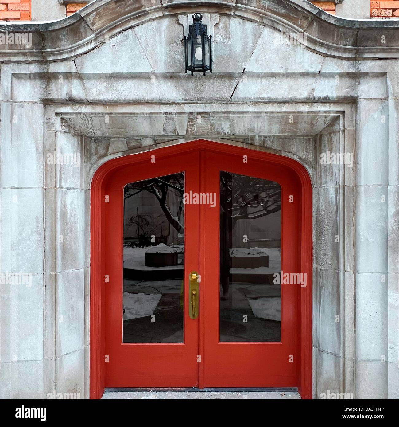 Doppie porte rosse in stile gotico con pannelli di vetro ad arco collocati all'interno di un ingresso in pietra resistente agli agenti atmosferici. - Immagine stock catturata con smartphone