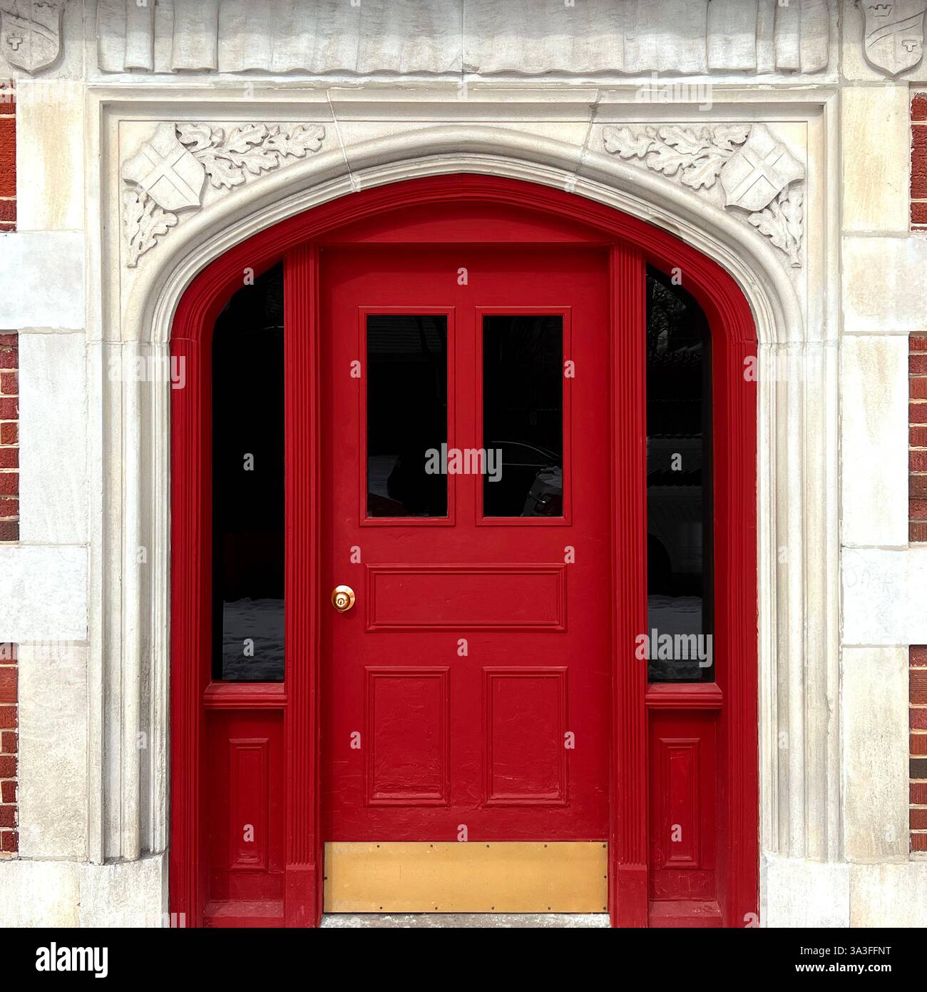 Porta ad arco rossa in stile gotico incorniciata da intricate incisioni in pietra in uno storico edificio in mattoni. - Immagine stock catturata con smartphone