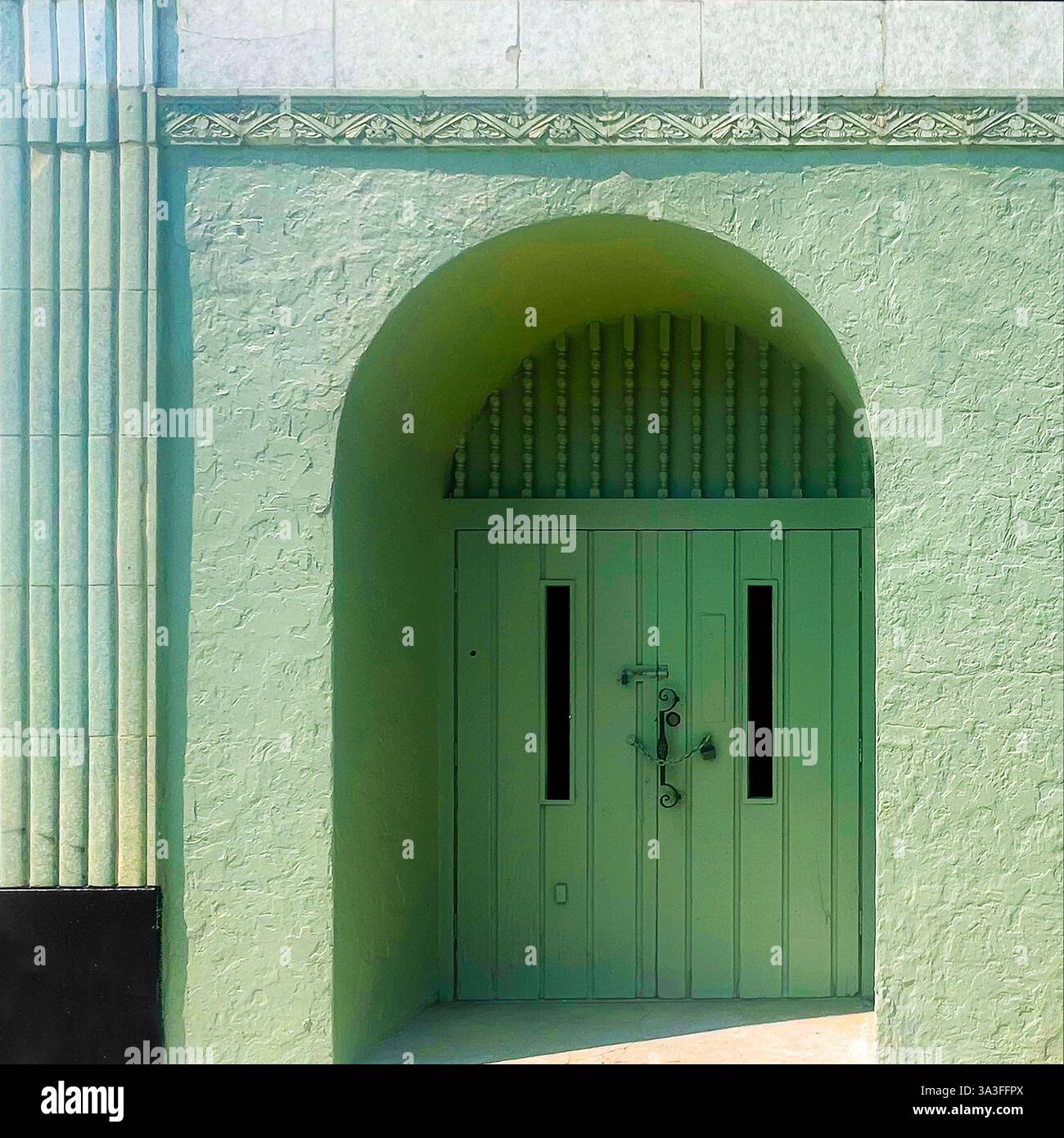 Porta d'ingresso ad arco verde menta vintage con dettagli in metallo ornato, collocata all'interno di una facciata testurizzata. - Immagine stock catturata con smartphone