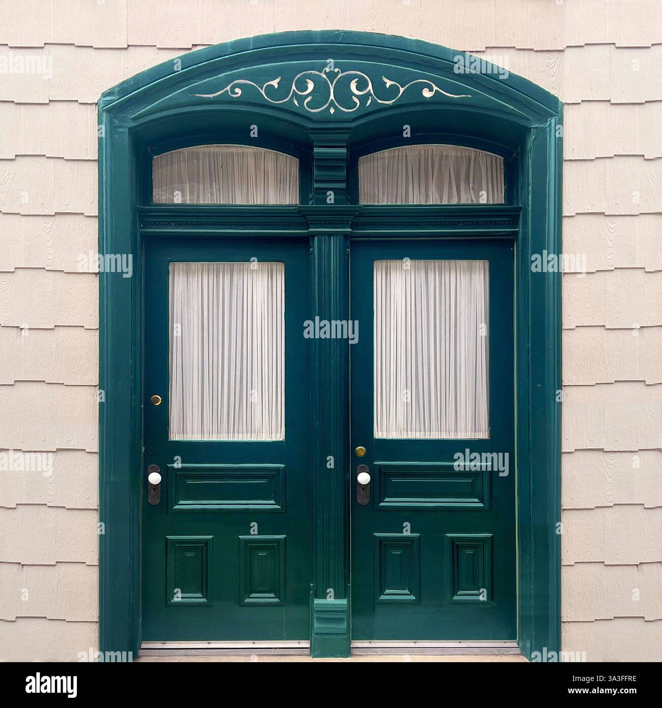 Eleganti doppie ante verde scuro con delicate tende bianche, incorniciate da un ingresso ad arco con dettagli decorativi. Foto Stock