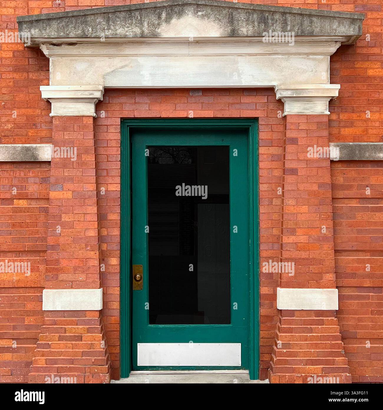 Ingresso architettonico caratterizzato da una porta verde profonda incorniciata da una facciata in mattoni rossi con accenti e frontone in pietra bianca. - Immagine stock catturata con smartphone