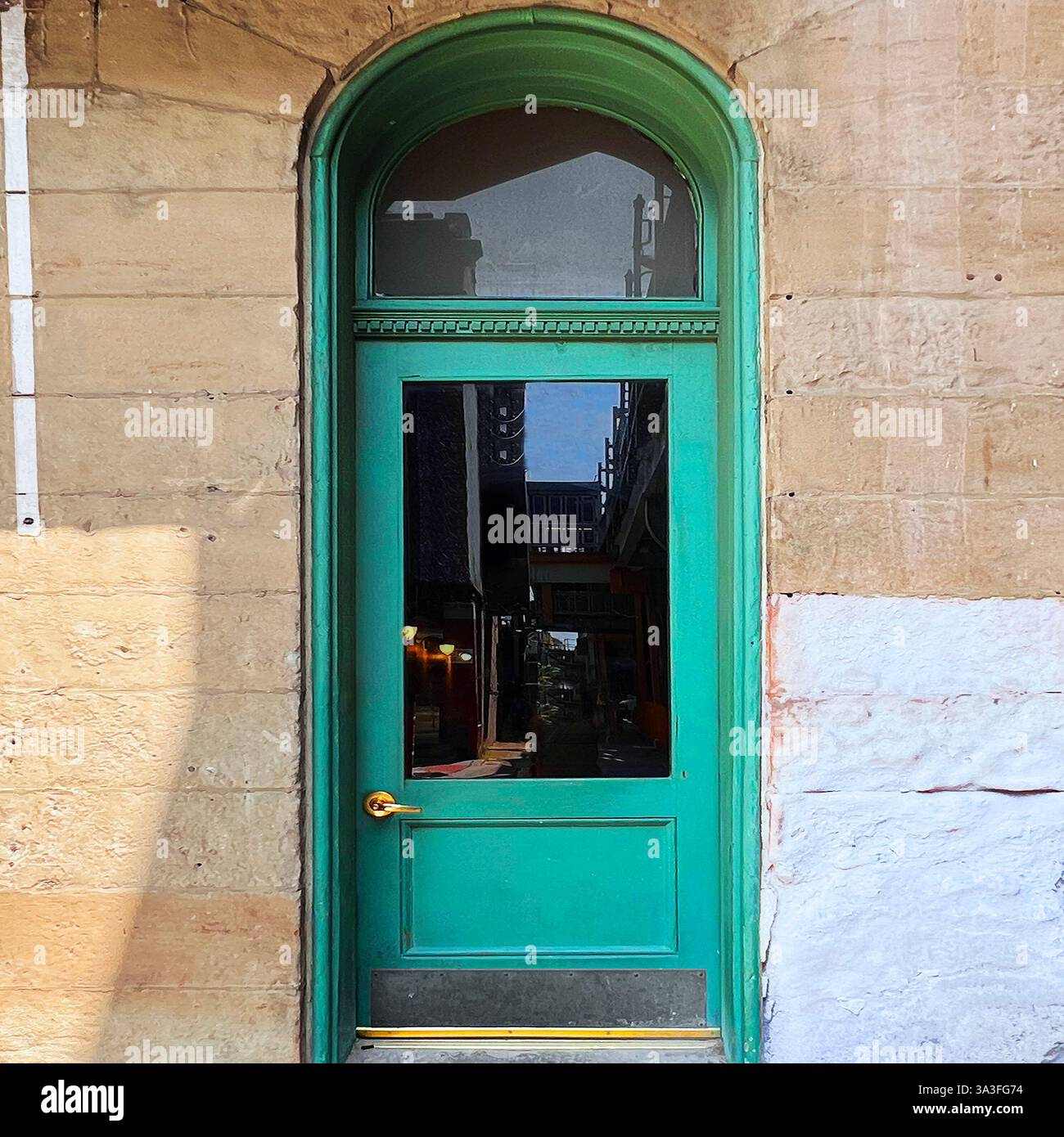 Porta ad arco alta dipinta di verde vibrante, che riflette gli edifici della città, adagiata in una storica facciata in pietra a Chicago - Immagine stock catturata con smartphone