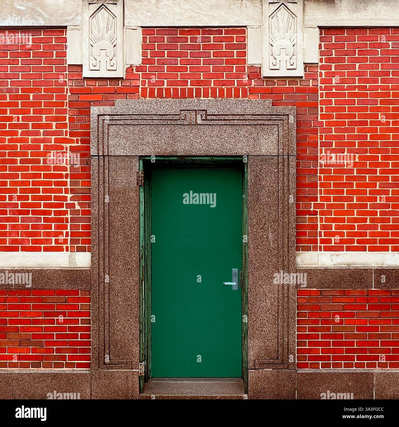Porta Art Deco con porta in metallo verde con dettagli geometrici in granito, circondata da mattoni decorativi rossi e pietra. - Immagine stock catturata con smartphone