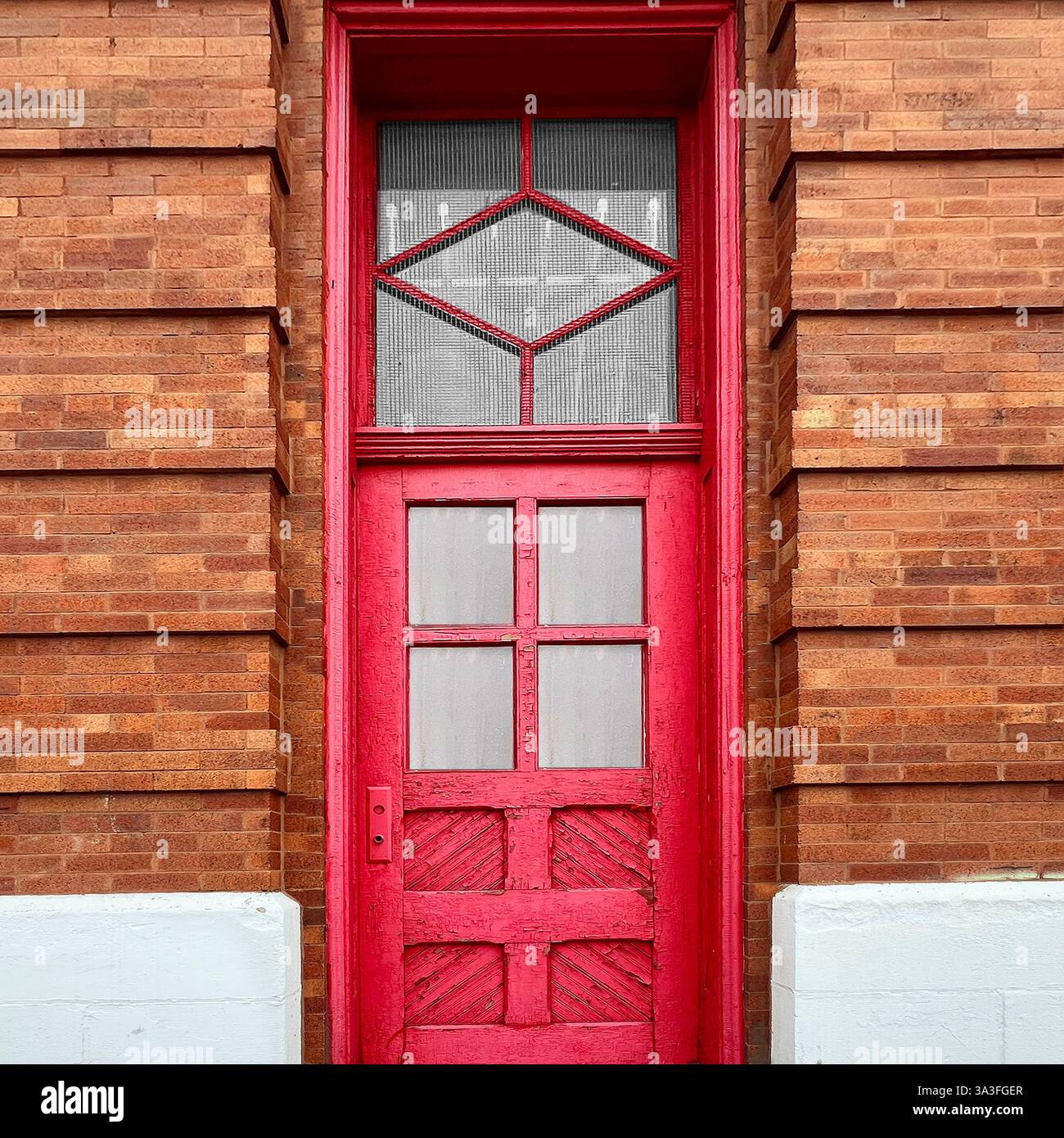 Porta urbana d'epoca caratterizzata da un'alta e vibrante porta in legno rosso con distintivi motivi geometrici delle finestre, incorniciata da dettagliati mattoni. - Immagine stock catturata con smartphone