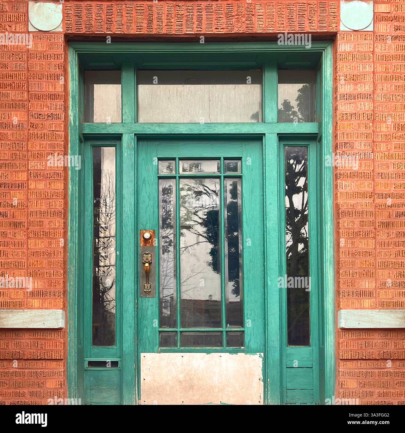 Una porta verde vintage con pannelli di vetro verticali adagiati su una facciata in mattoni arancioni a Chicago. Foto Stock