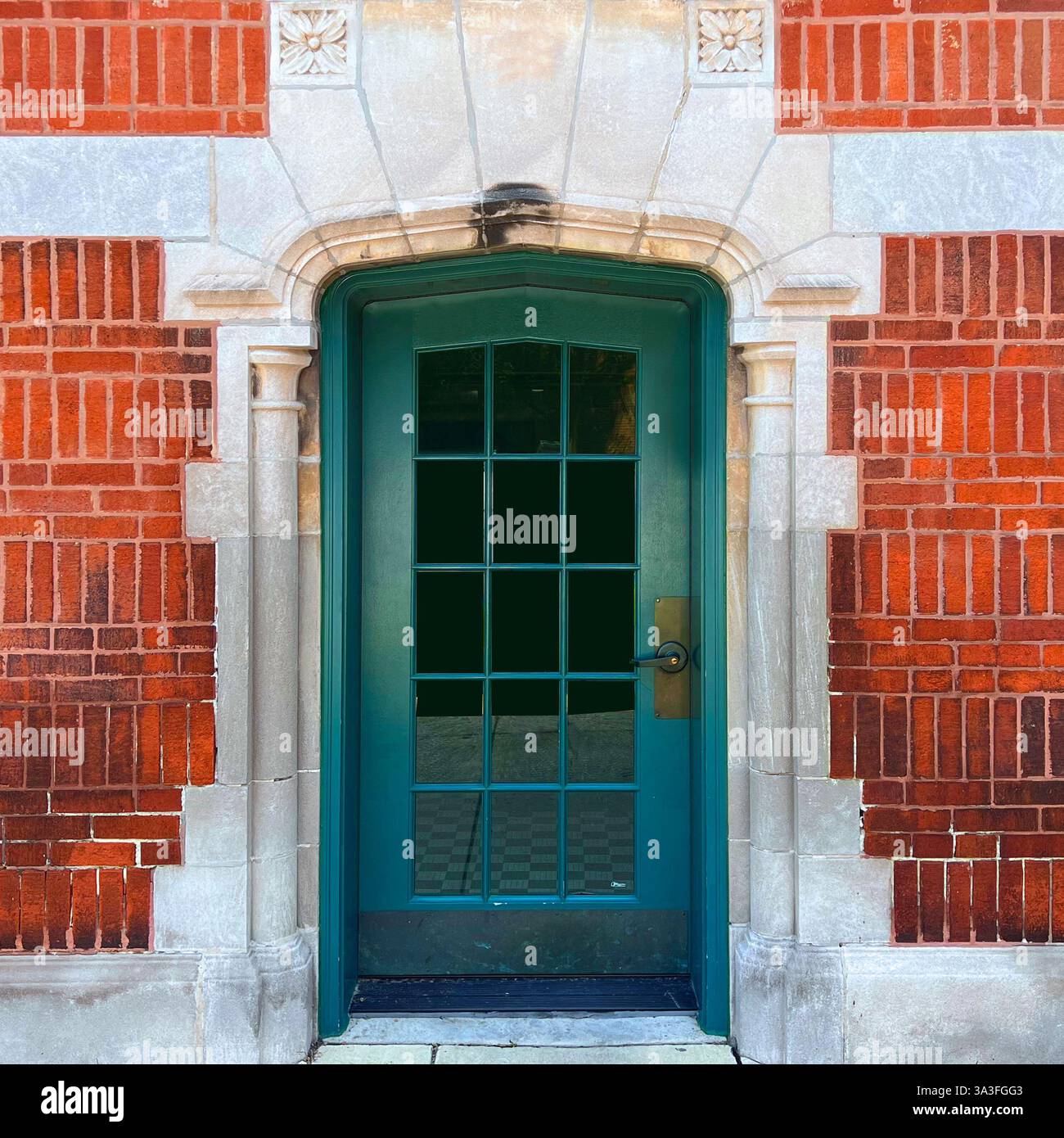 Porta con pannelli di vetro verde posta all'interno di un arco in pietra in stile gotico caratterizzato da intricate incisioni, incorniciate da una facciata in mattoni arancioni a Chicago. - Immagine stock catturata con smartphone