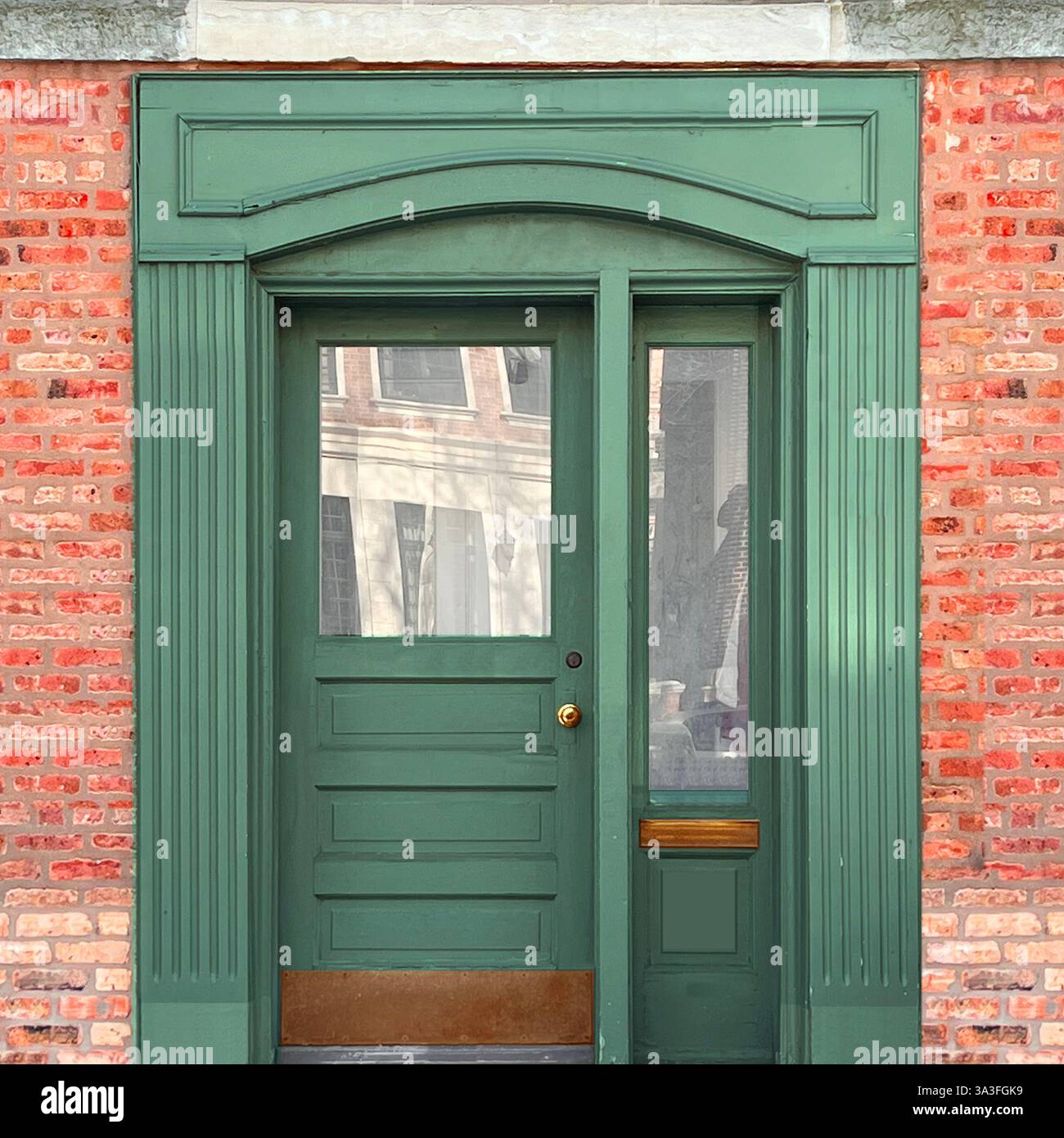 Elegante porta in legno verde con pannelli in vetro, hardware in ottone e una cornice decorativa ad arco collocata in una facciata in mattoni rosa a Chicago. Foto Stock