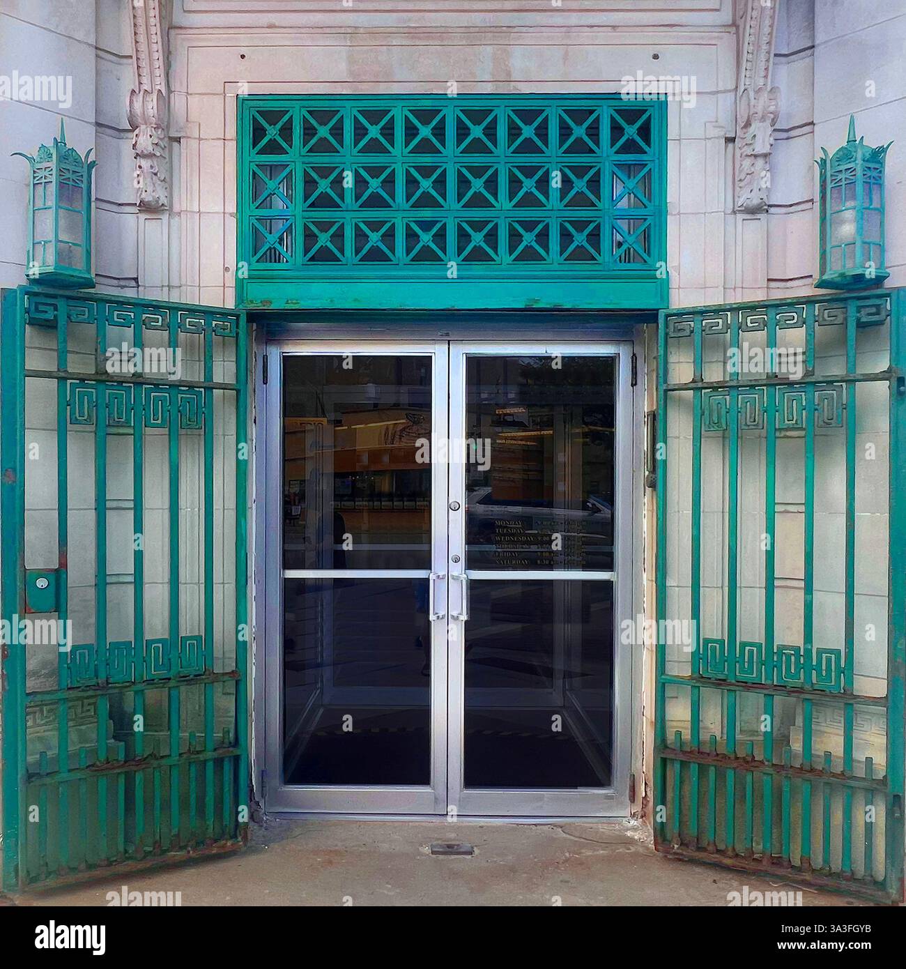 Un ingresso storico sulla riva caratterizzato da una porta in vetro argentato incorniciata da cancelli di metallo verde e da un reticolato, adagiato all'interno di una classica facciata in pietra. - Immagine stock catturata con smartphone