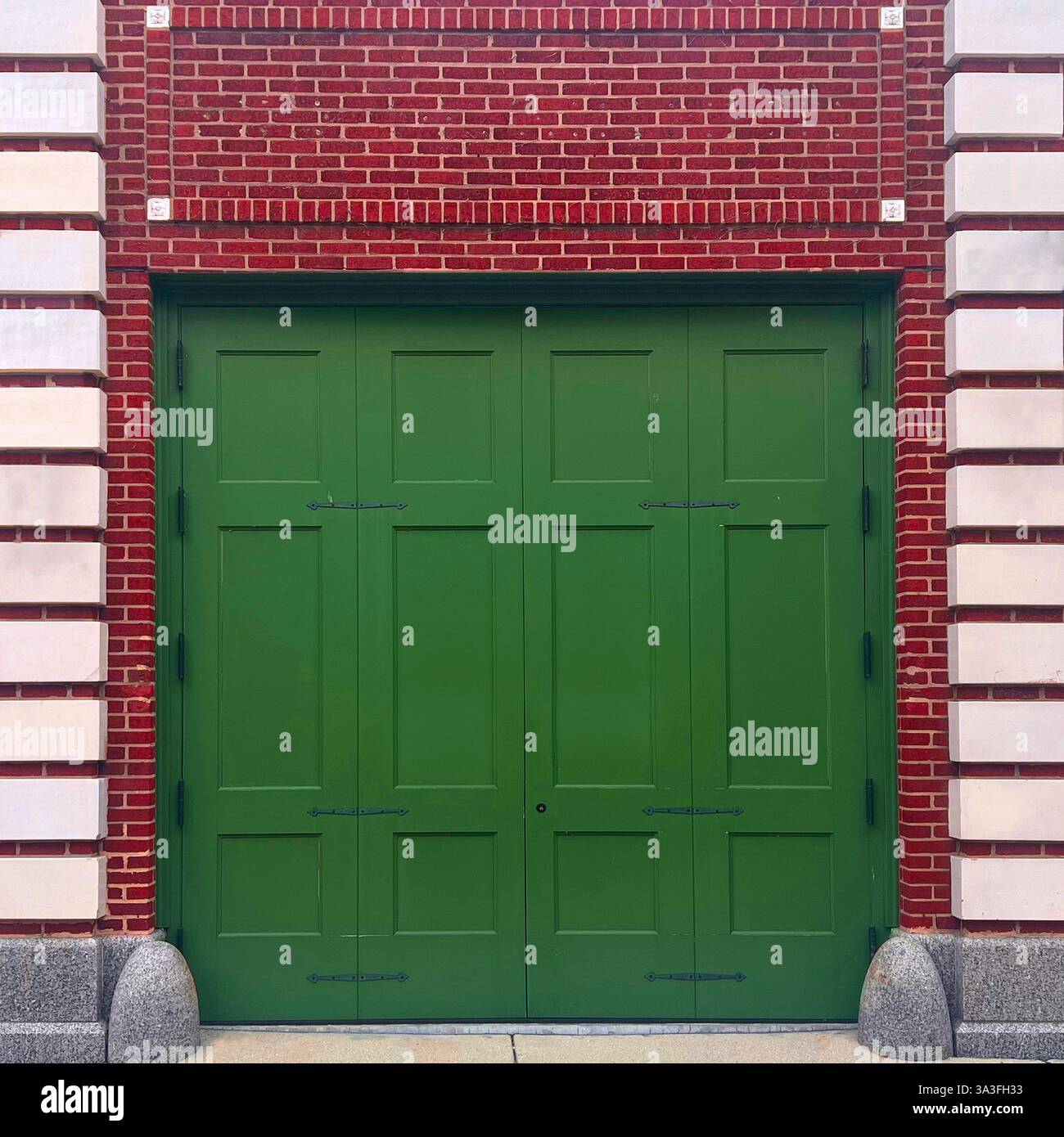 Una storica porta verde in stile carrozza posta all'interno di una facciata in mattoni rossi e pietra calcarea a Chicago. - Immagine stock catturata con smartphone