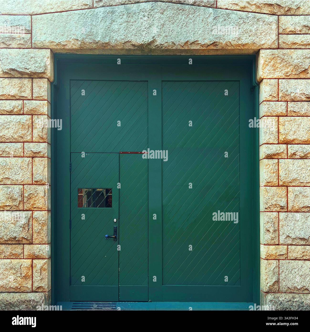 Una grande porta del garage in legno verde con pannelli diagonali, adagiata all'interno di una storica facciata in pietra della Glessner House, un punto di riferimento architettonico di Chicago. - Immagine stock catturata con smartphone