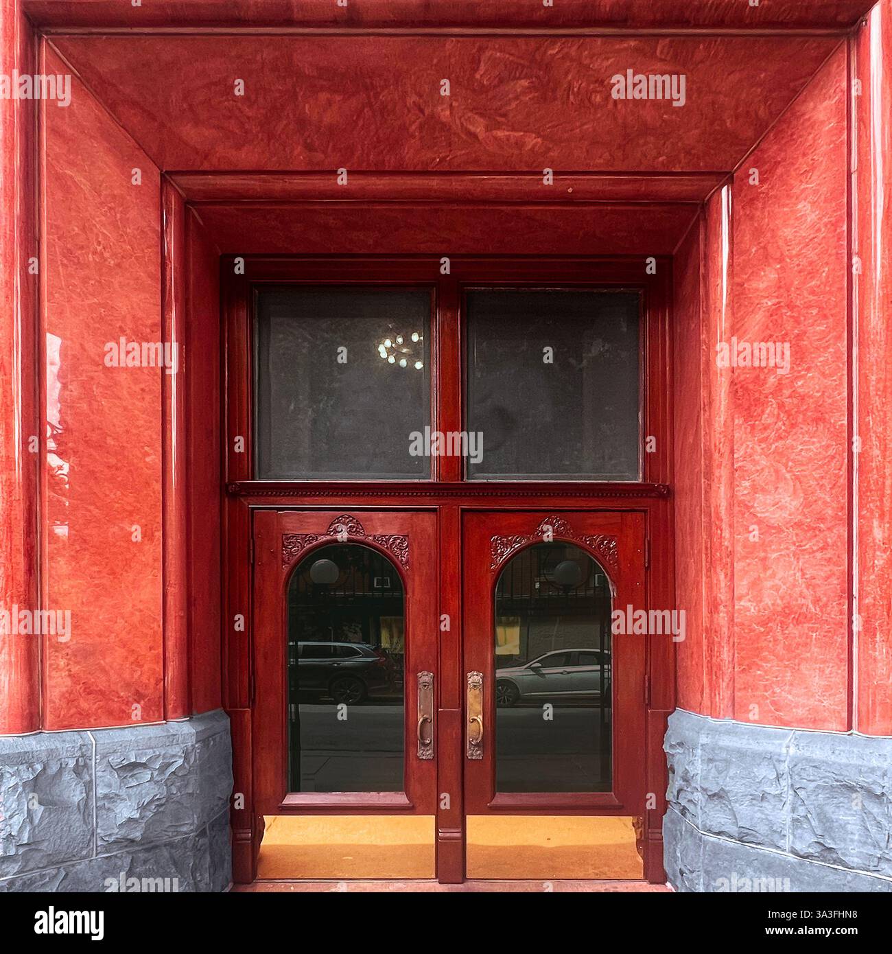 Doppia porta rossa con decorazioni in legno collocate all'interno di una facciata in marmo rosso lucido, che riflette l'eleganza dell'architettura storica di Chicago Foto Stock