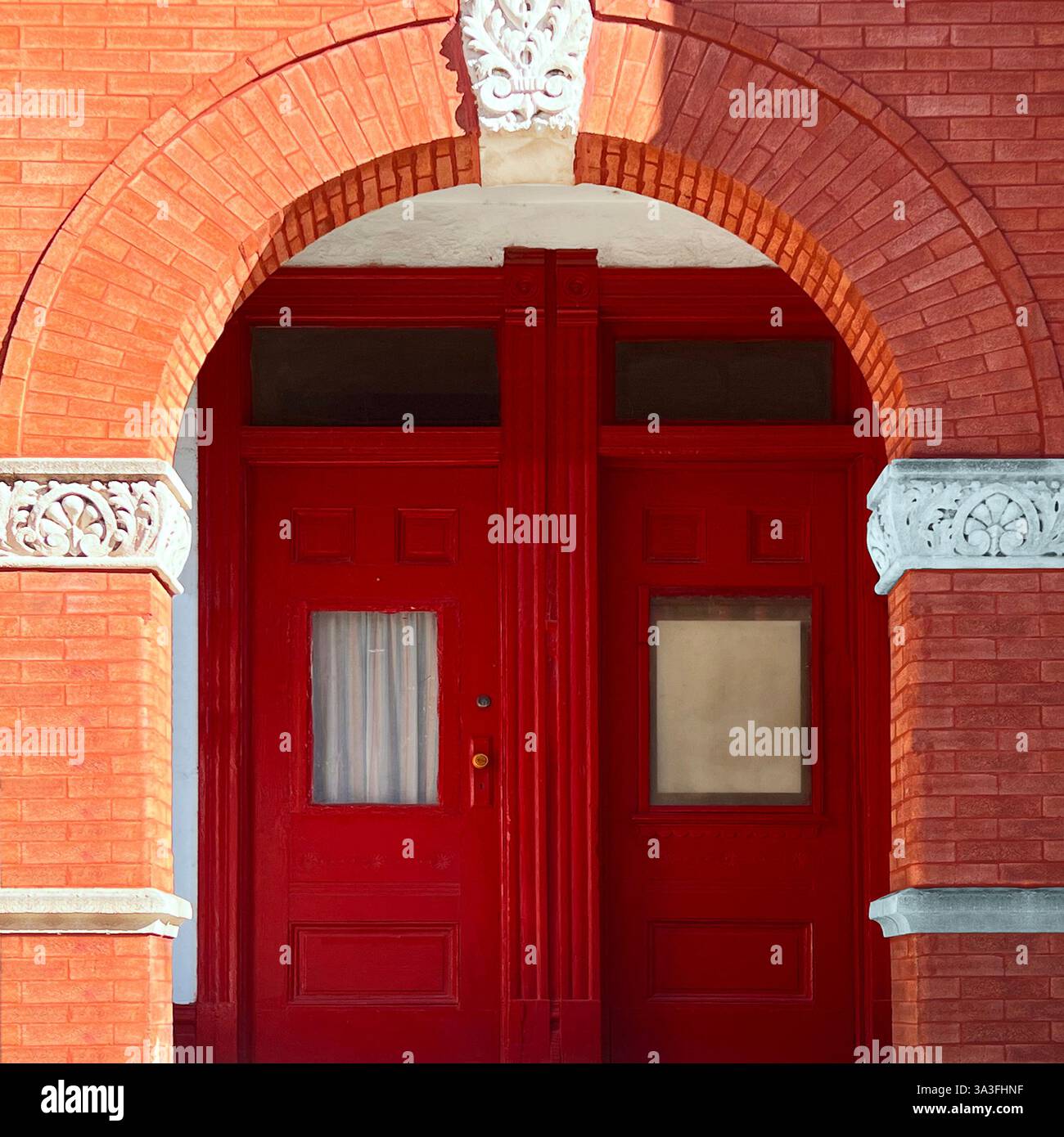 Doppia porta rossa incorniciata da un grande ingresso in mattoni ad arco con intricati dettagli in pietra. - Immagine stock catturata con smartphone