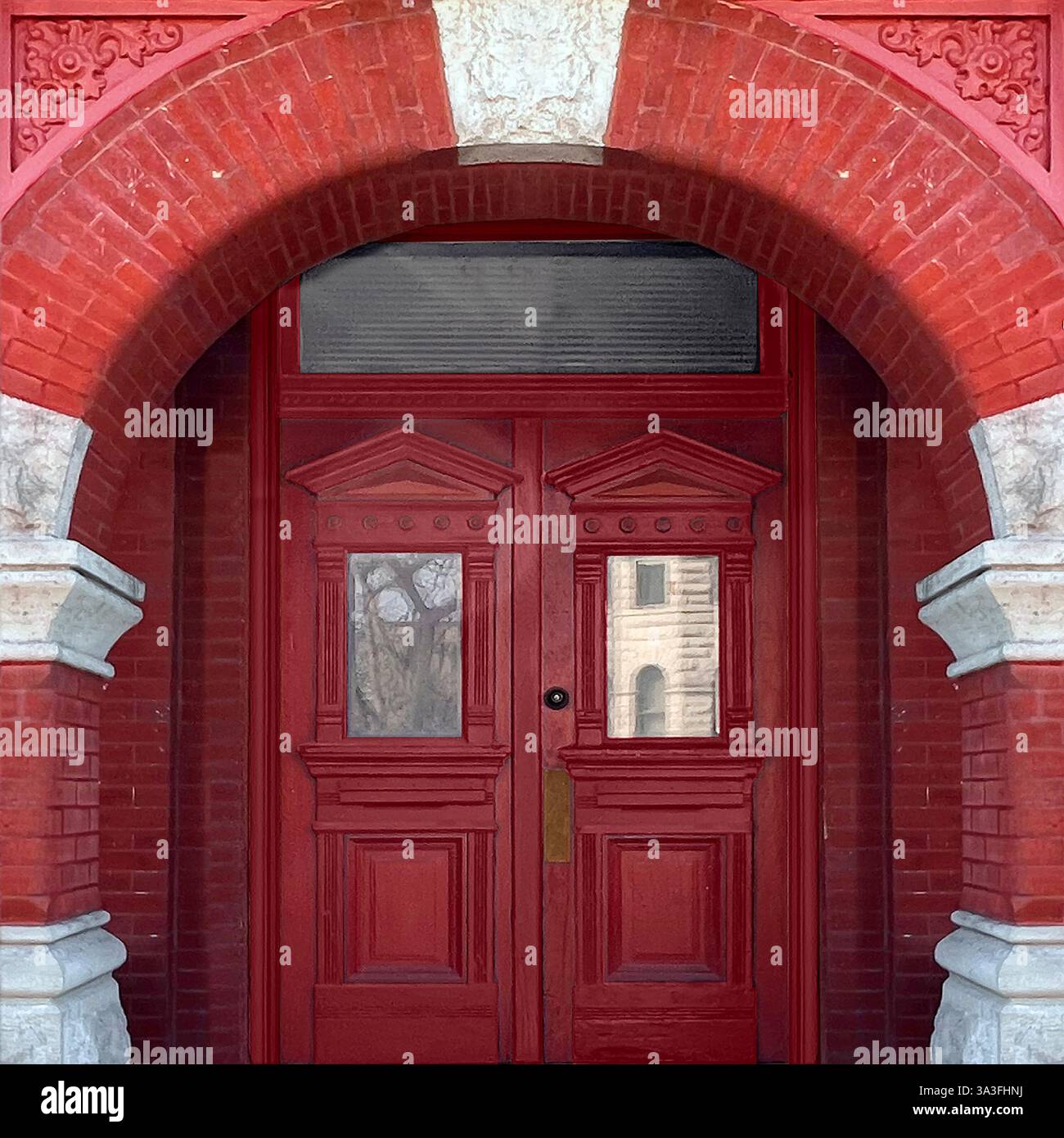 Doppia porta rossa riccamente dettagliata incorniciata da un audace ingresso in mattoni ad arco, con pannelli geometrici e dettagli in pietra a contrasto Foto Stock