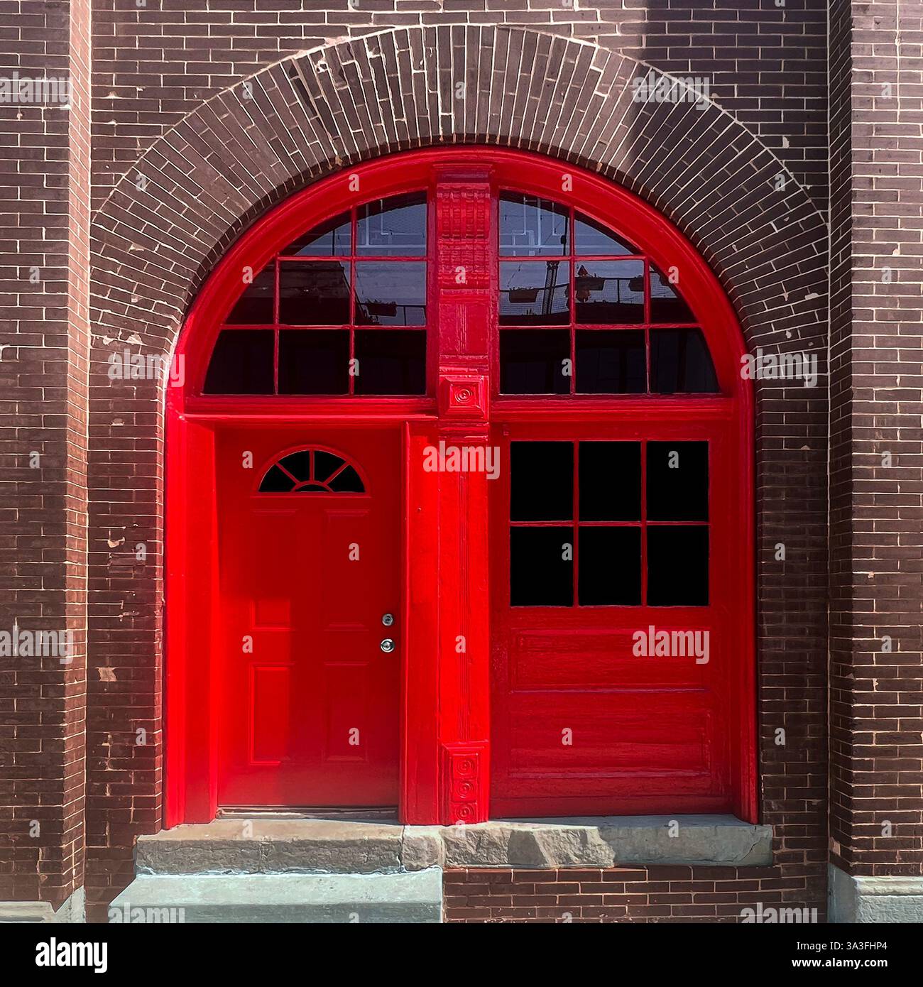 Porta ad arco di colore rosso brillante con pannelli adiacenti collocati in un edificio di mattoni marroni, caratterizzato da un contrasto sorprendente tra architettura e colore Foto Stock