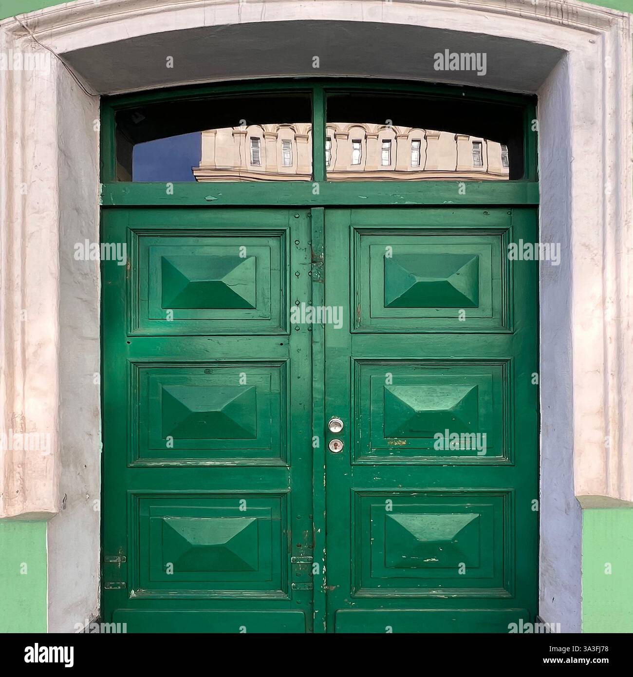 Una suggestiva porta doppia in legno verde con pannelli geometrici e una finestra a specchio di poppa ad arco, che riflette uno storico stile architettonico europeo a Kraków - Immagine stock catturata con smartphone