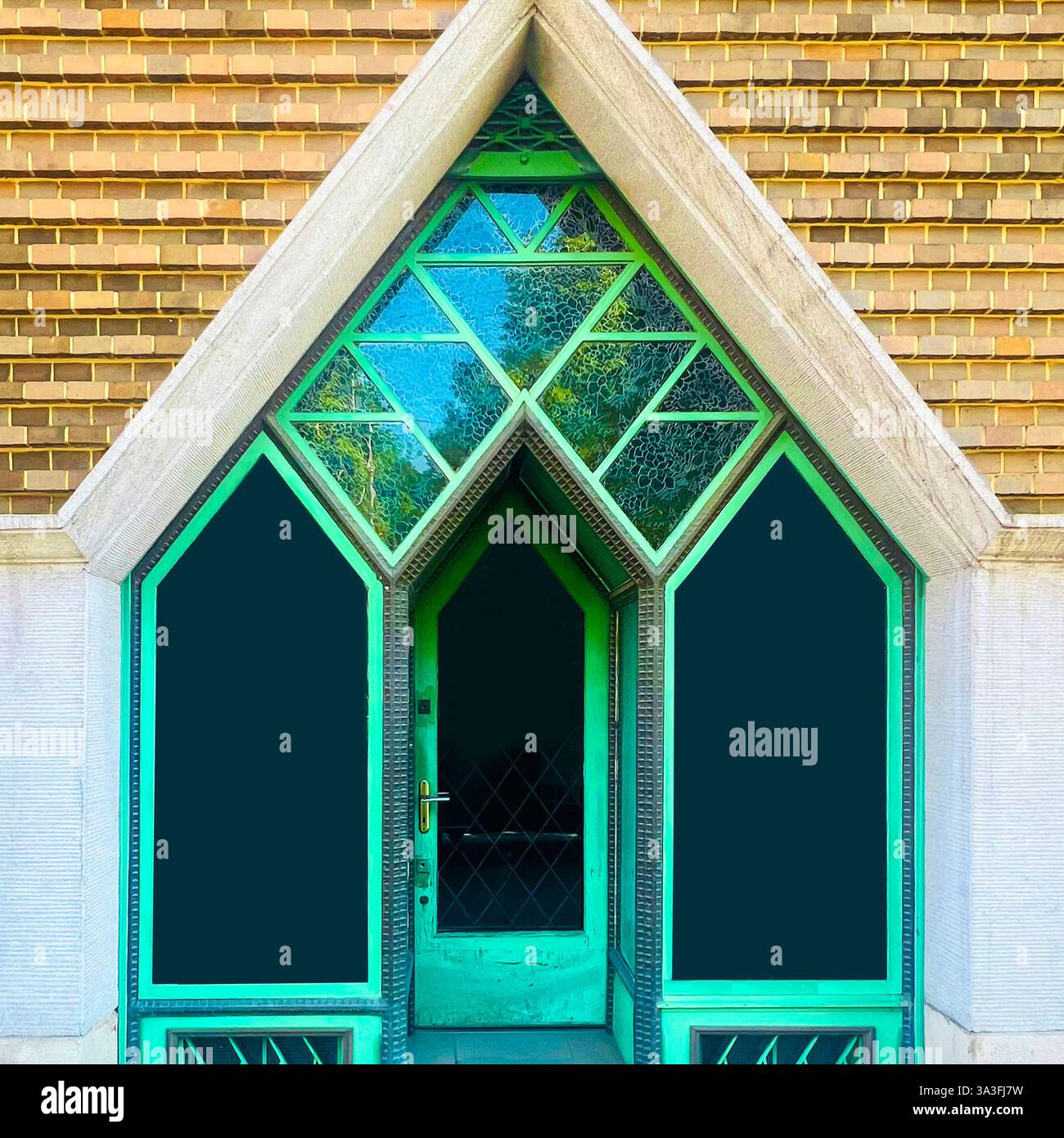 Porta geometrica verde con finestre in vetro colorato all'interno di una cornice triangolare in pietra, che mostra un design architettonico moderno a Kraków, Polonia - Immagine stock catturata con smartphone