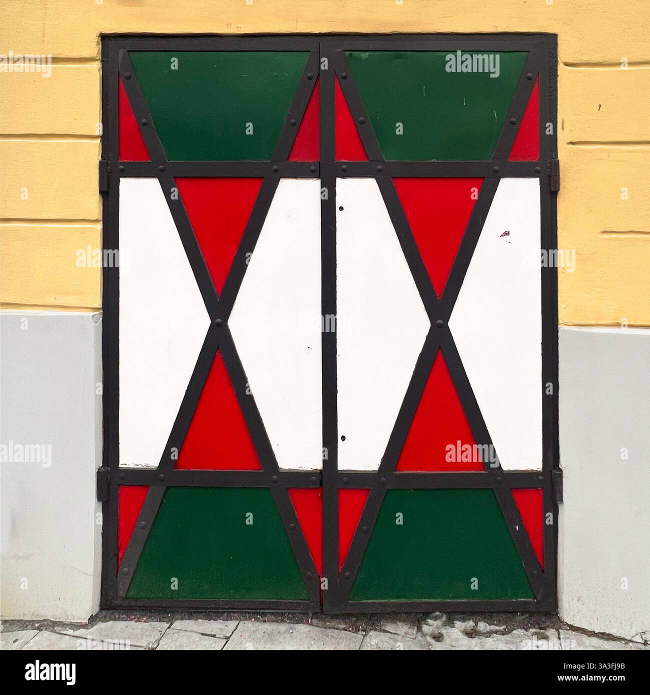 Porta in metallo con motivi geometrici in rosso, bianco e verde, adagiata su un muro giallo e grigio a Varsavia, Polonia Foto Stock