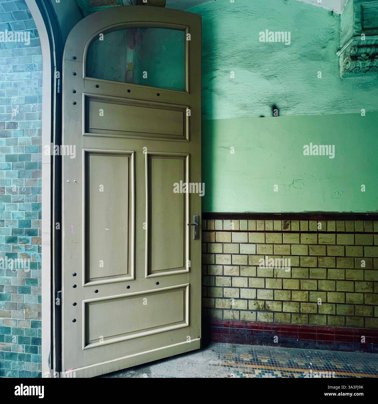 Una porta in legno invecchiato si apre leggermente in un vecchio edificio con pareti verdi e piastrelle vintage a Breslavia, Polonia - Immagine stock catturata con smartphone