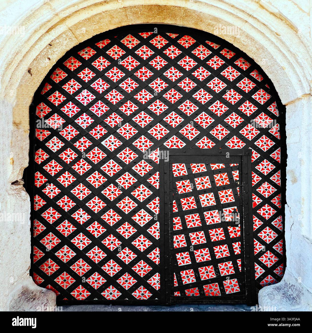 Porta medievale con fantasie complesse nella città vecchia di Cracovia, Polonia, caratterizzata da cancello di ferro nero dimond con motivi floreali rossi adagiati all'interno di una pietra - Immagine stock catturata con smartphone