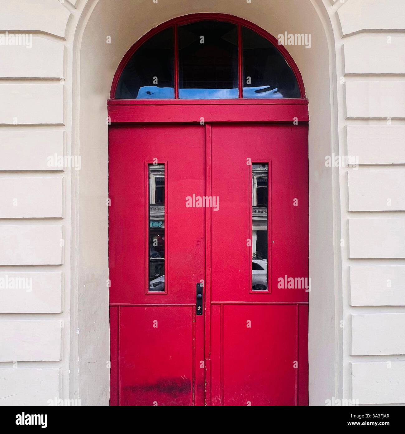 Doppia porta rossa con finestre strette e specchio di poppa ad arco, situata in una classica facciata color crema a Łódź, Polonia Foto Stock