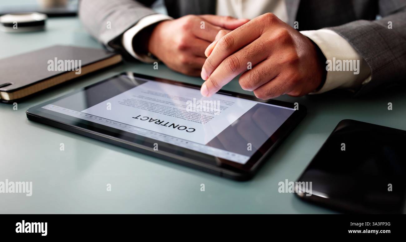 Giovane concentrato che esamina i documenti contrattuali sul computer in ufficio. Foto Stock