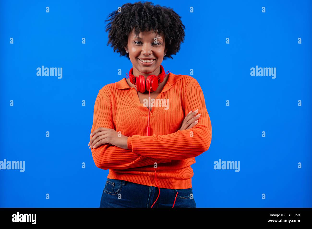 Donna afro-americana sorridente con cuffie rosse in posa su sfondo blu Foto Stock