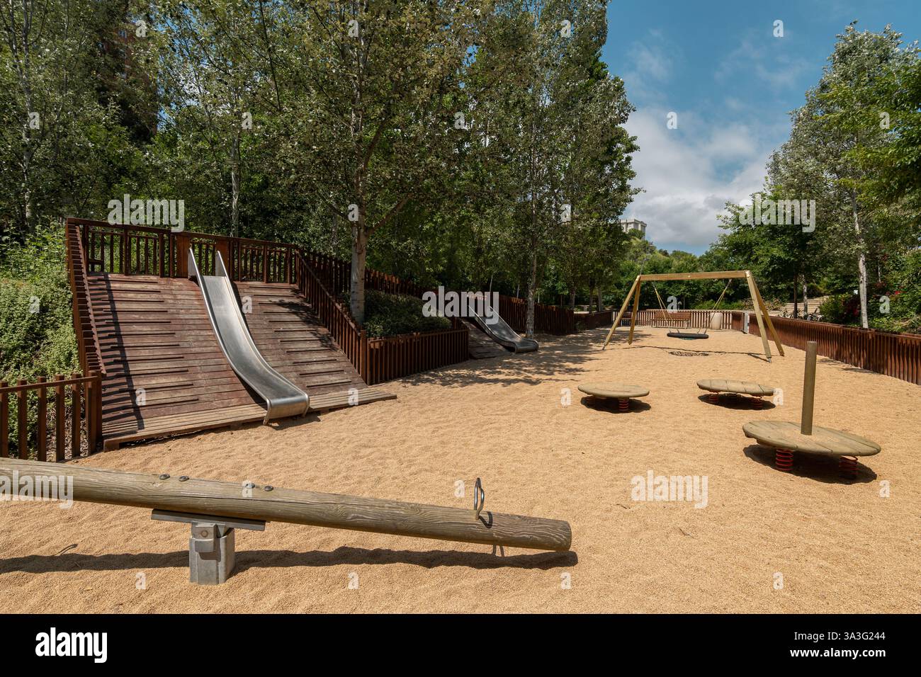 Parco giochi per bambini con scivoli, altalene e strutture in legno circondate da alberi Foto Stock