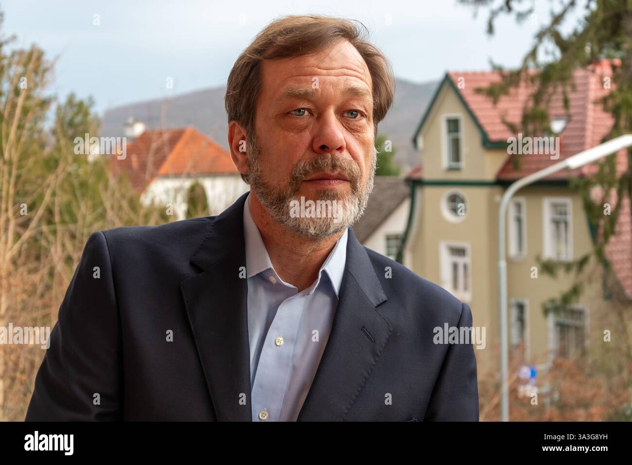 Ritratto di un uomo maturo in una tuta classica sullo sfondo di vecchie case e natura Foto Stock
